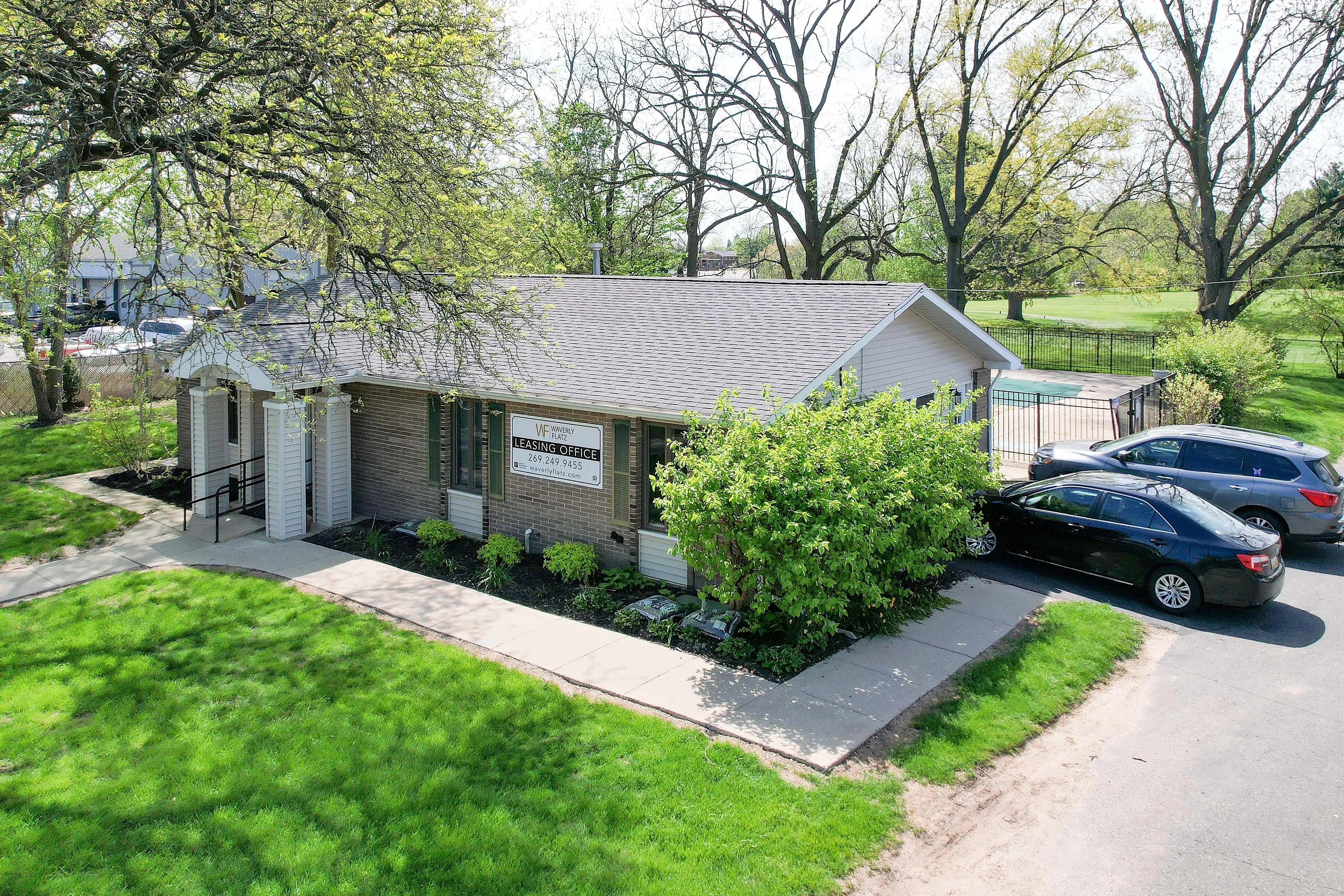 Charming leasing office nestled among lush greenery with convenient parking and inviting entrance.