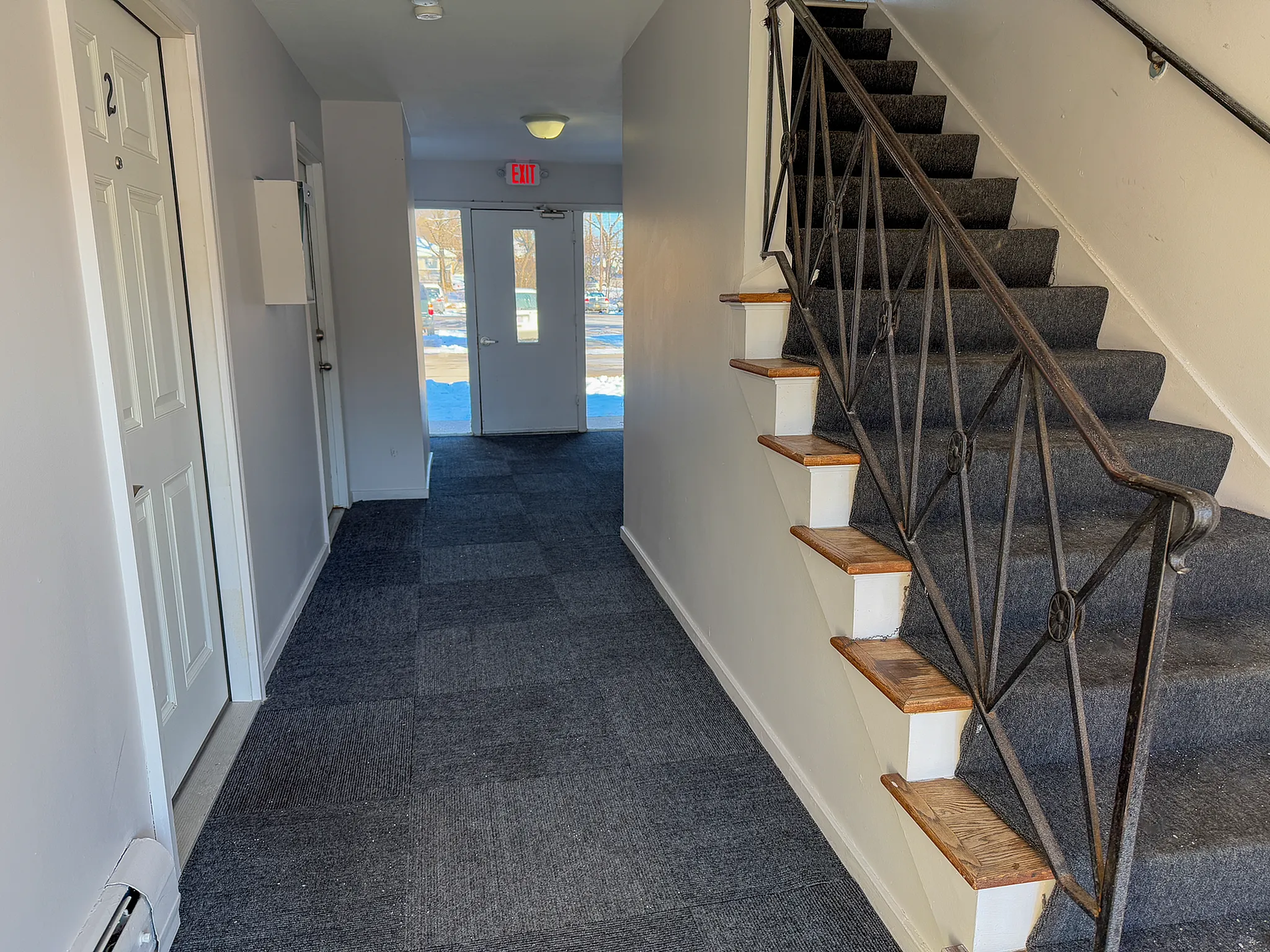 Bright apartment hallway with modern carpet, elegant staircase, and inviting natural light from glass door.