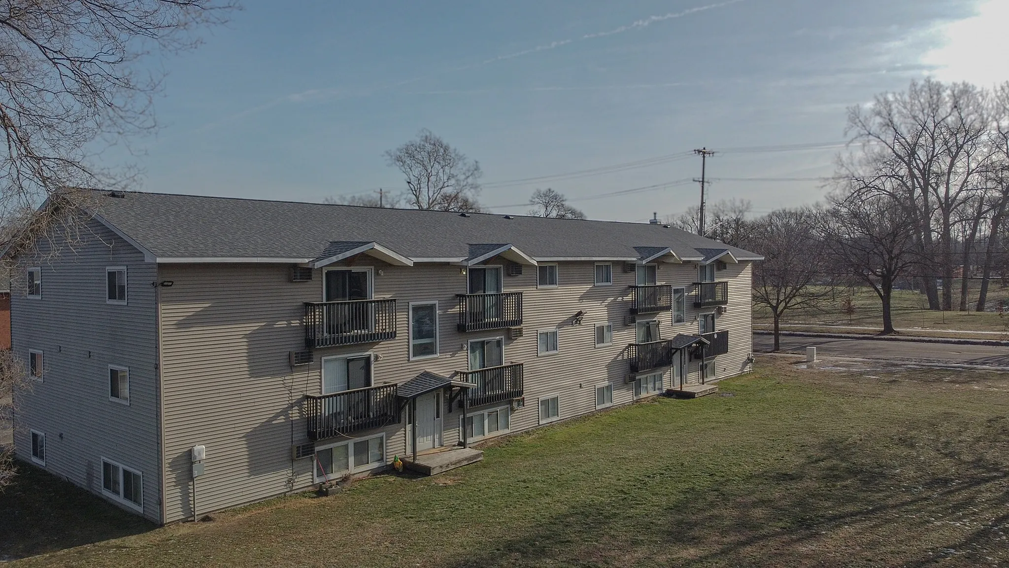 Inviting three-story apartment building with modern balconies and a spacious lawn, nestled in a serene neighborhood.