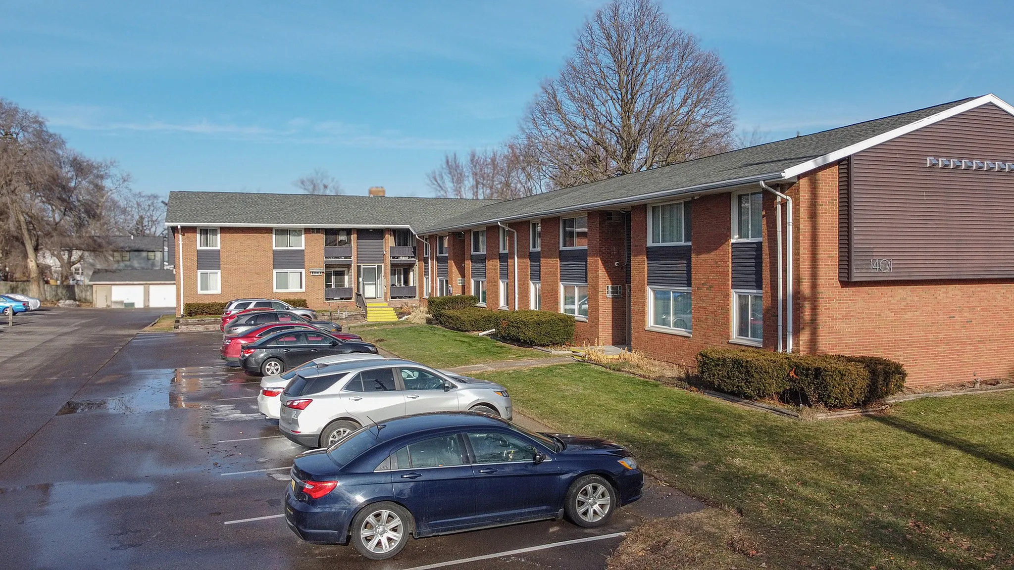 Charming red brick apartment complex with ample parking and landscaped greenery, perfect for convenient and comfortable living.