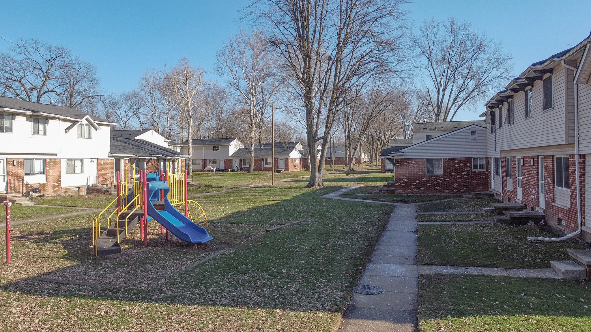 Charming apartment complex with a vibrant playground nestled among lush trees, perfect for family living in a friendly community.