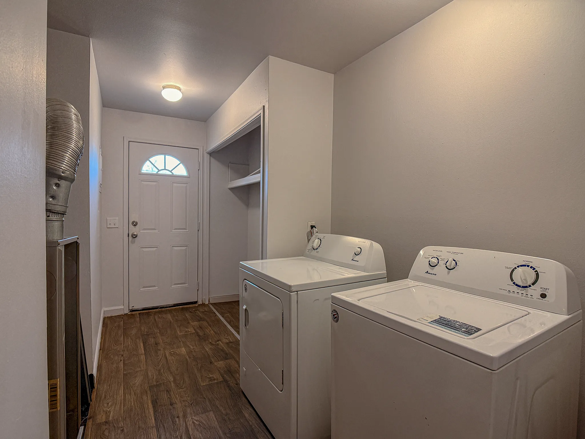 Modern laundry area with sleek washer and dryer, featuring elegant wood flooring and ample shelving, leading to a chic entrance door.