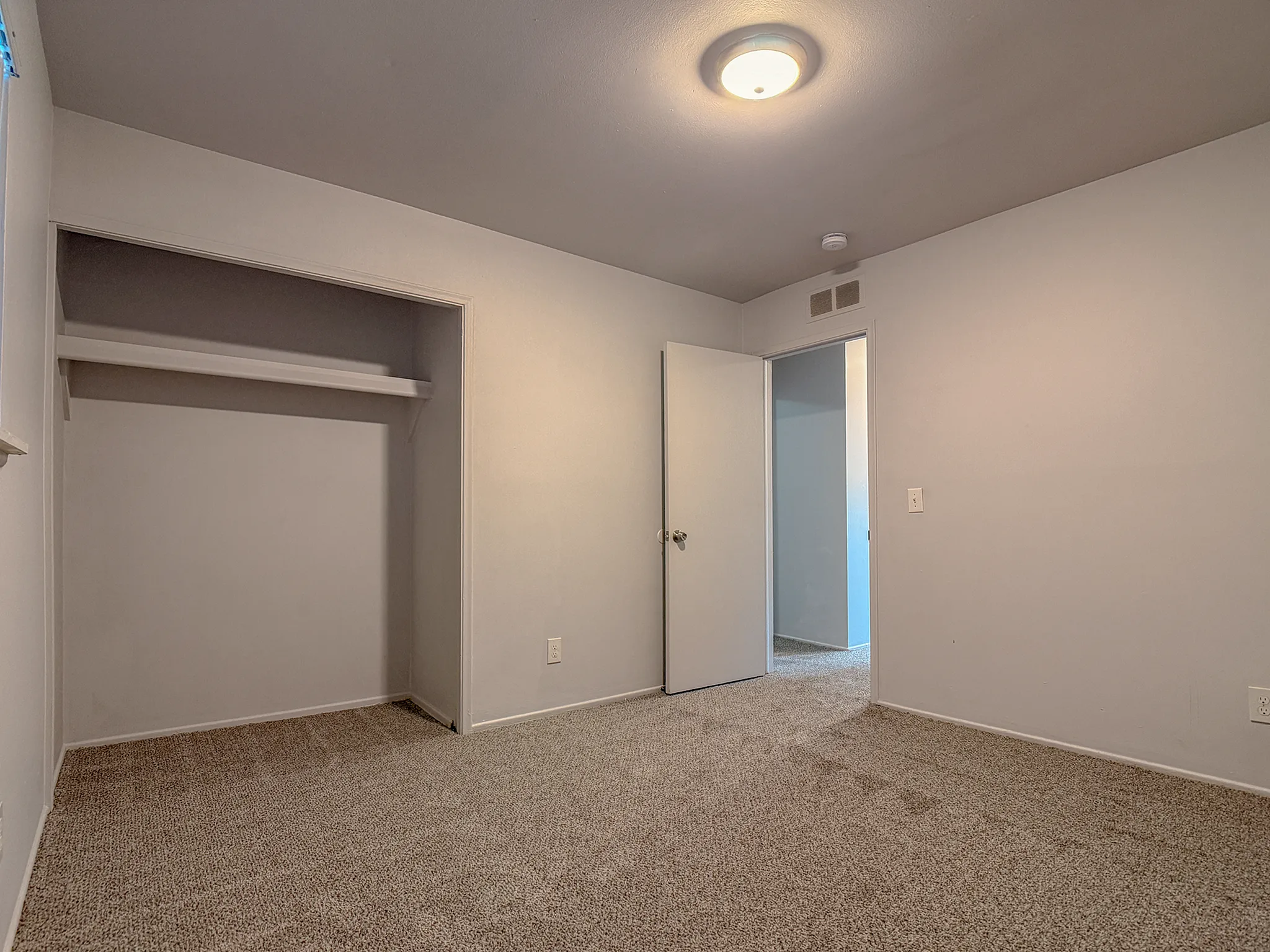 Inviting empty bedroom with soft carpet flooring, open closet space, and modern overhead lighting.
