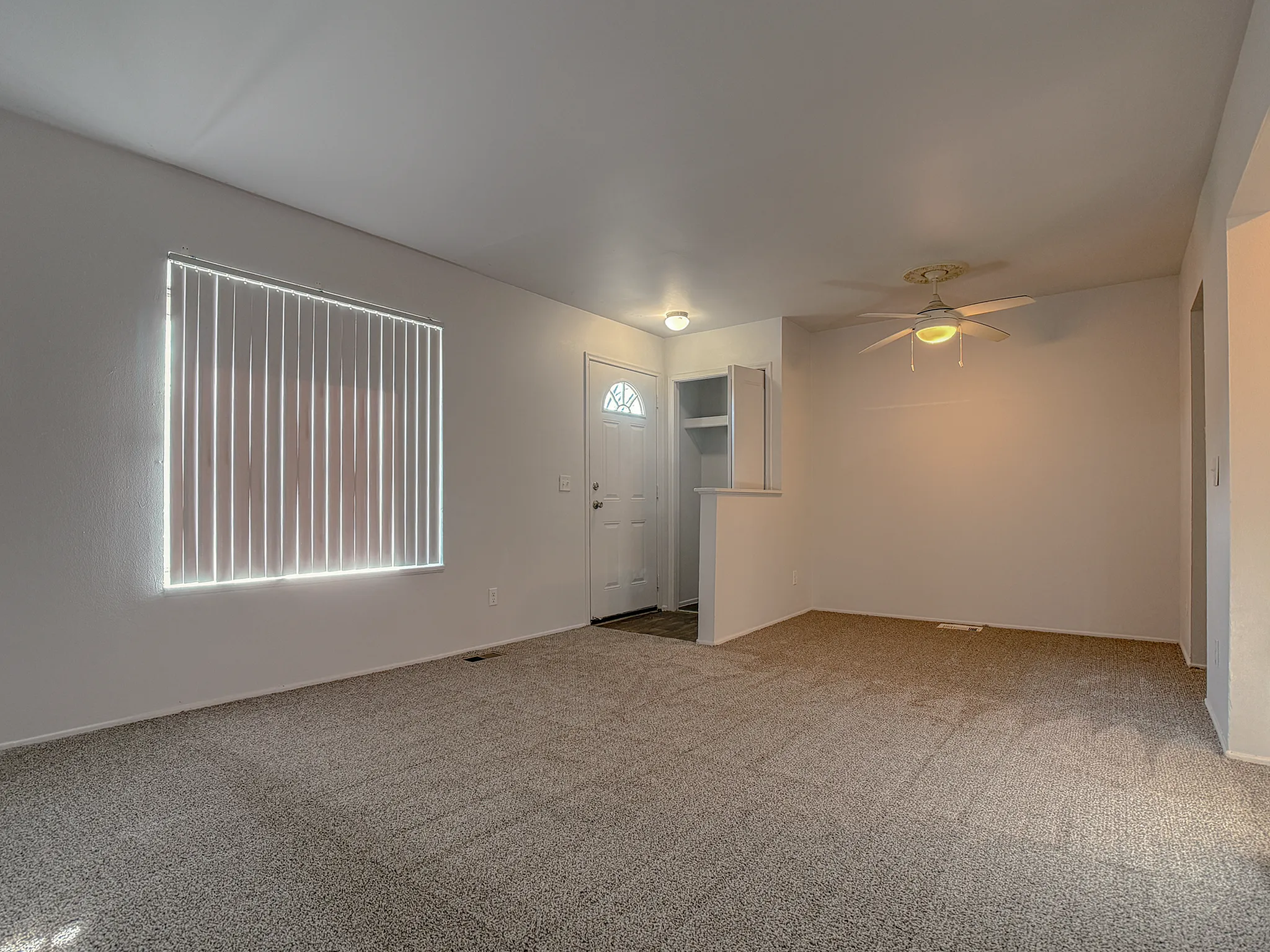 Inviting living room featuring soft carpeting, large window with vertical blinds, and a cozy ceiling fan.