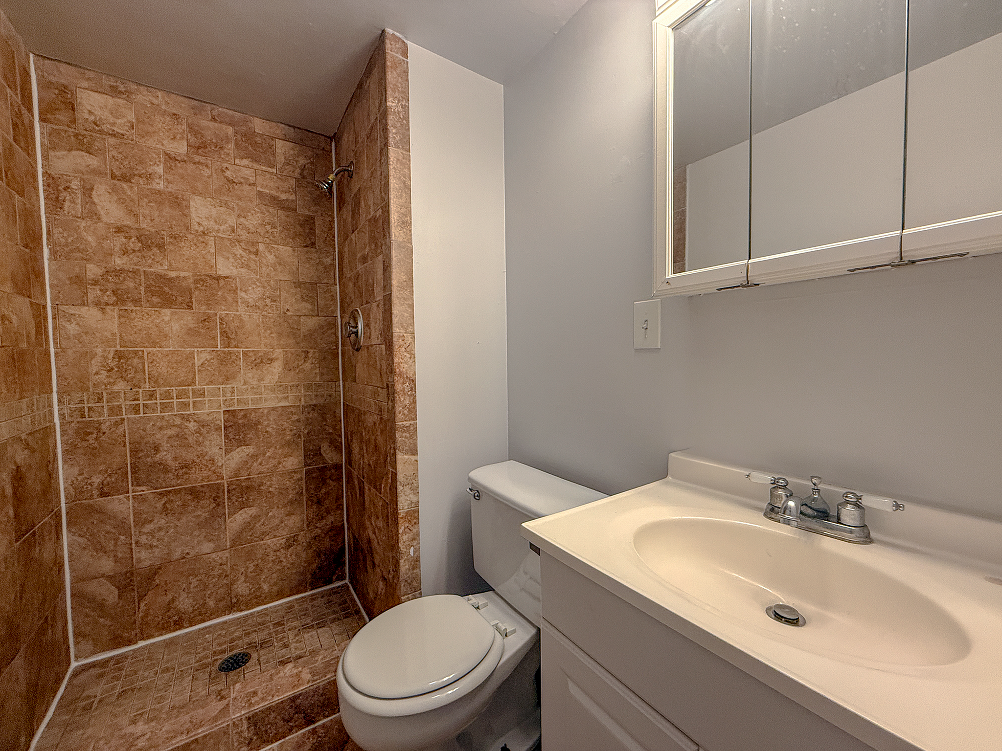 Modern bathroom featuring elegant stone-tiled shower, sleek vanity, and ample storage space.