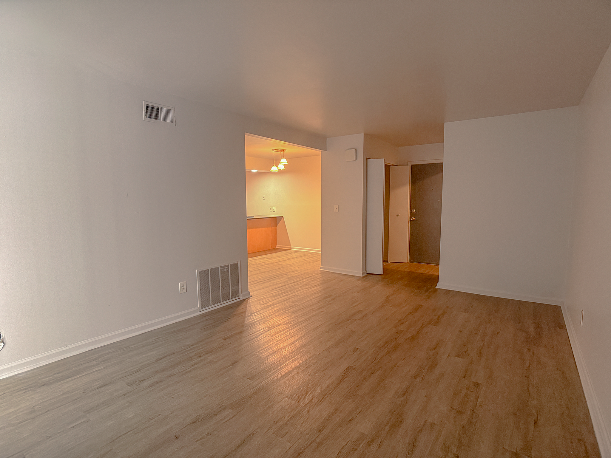 Inviting open-plan apartment with elegant hardwood floors, ambient lighting, and a spacious living area transitioning into a cozy kitchen.