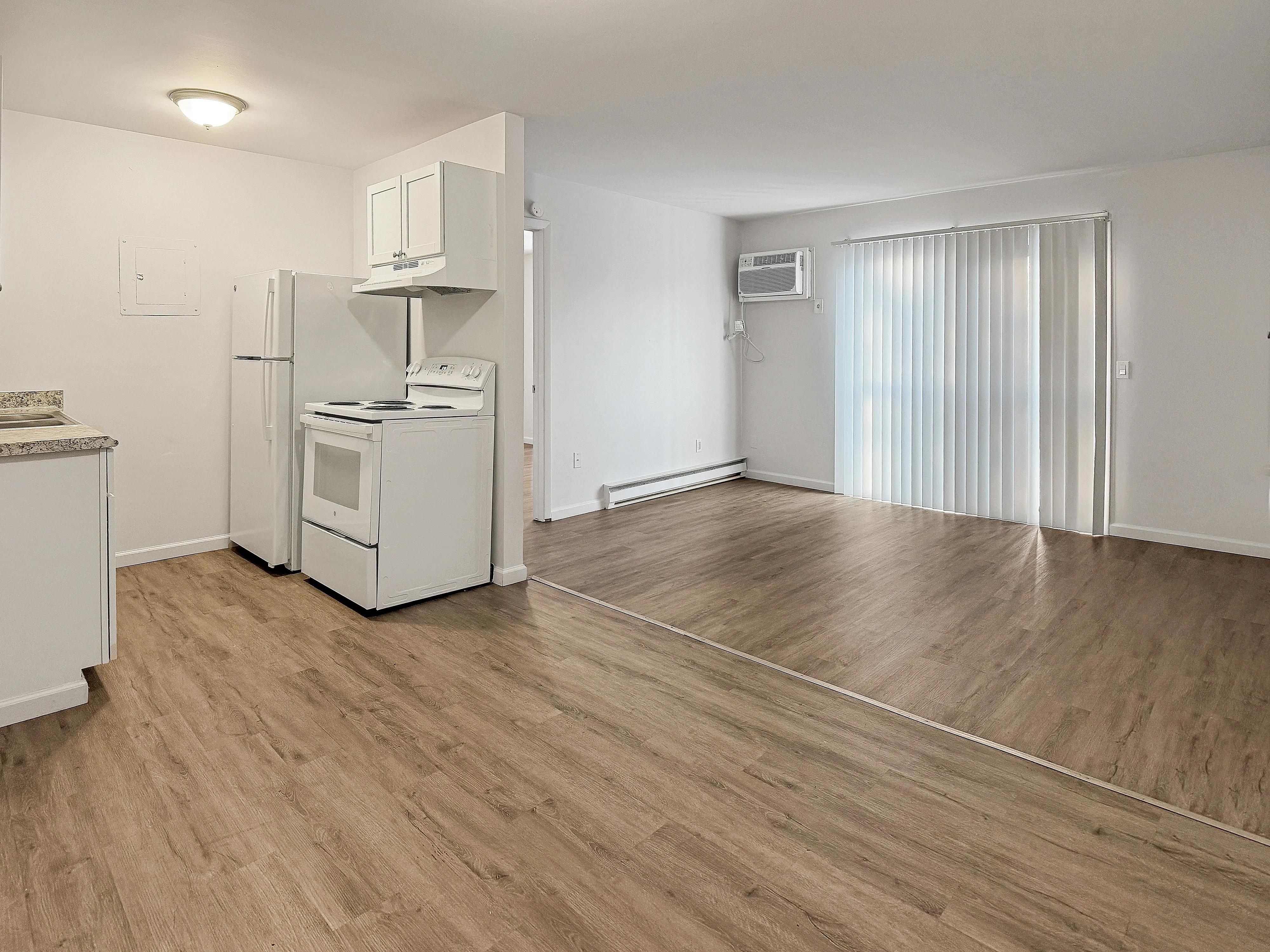 Modern open-plan apartment featuring sleek laminate flooring, a bright kitchen with updated appliances, and spacious living area with vertical blinds.