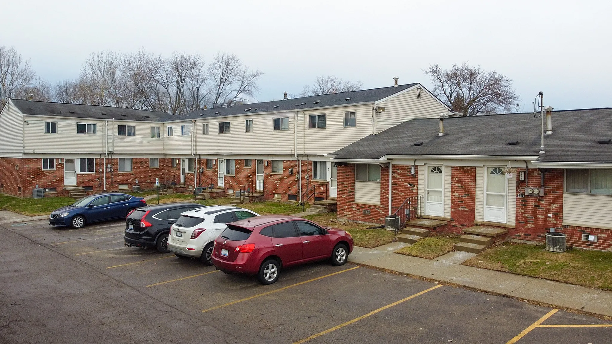Charming townhouse complex with red brick exterior, crisp white trim, and ample parking in a tranquil suburban setting.