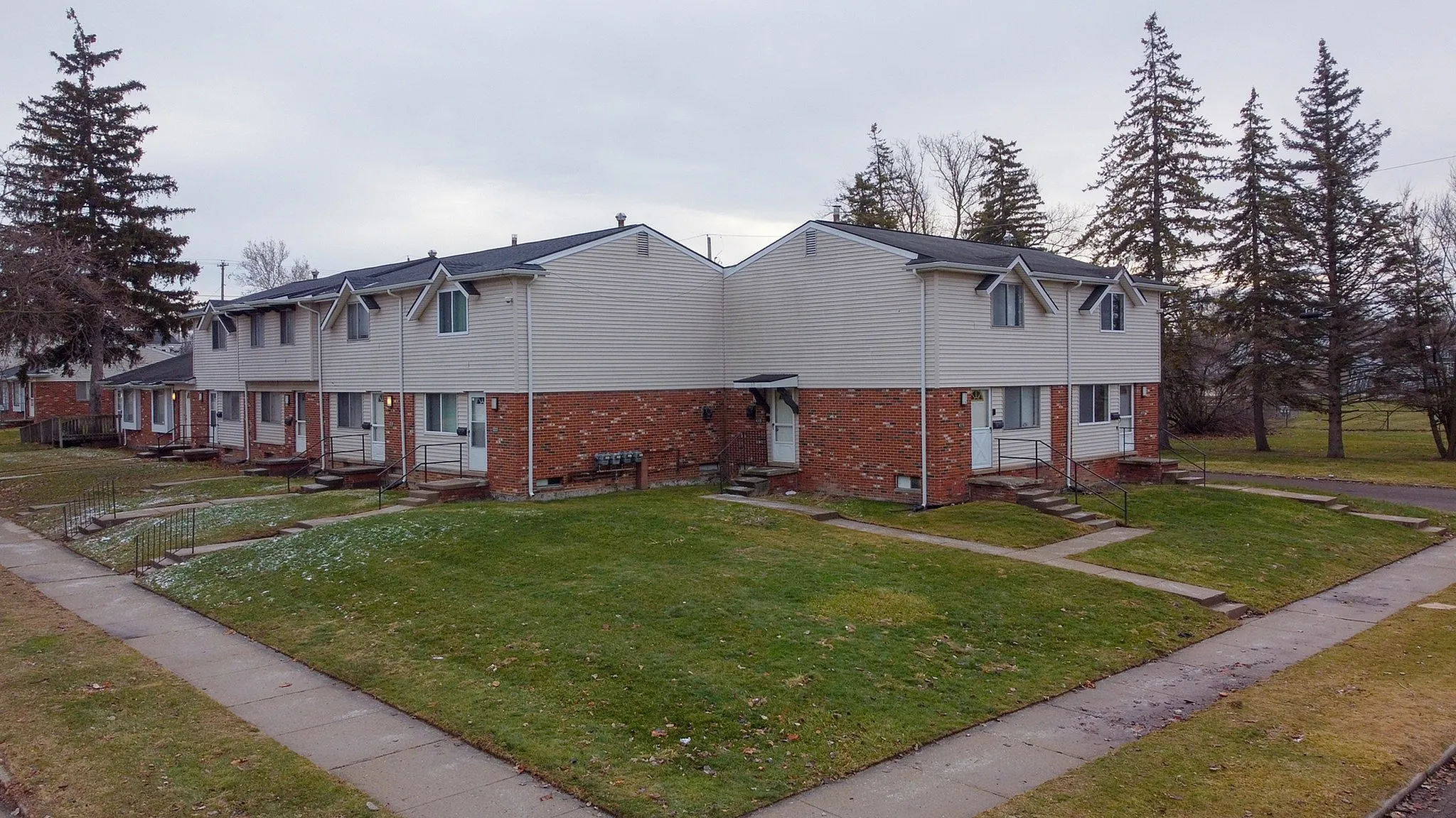 Charming townhouses with brick and siding exterior, surrounded by lush green lawns, perfect suburban living.