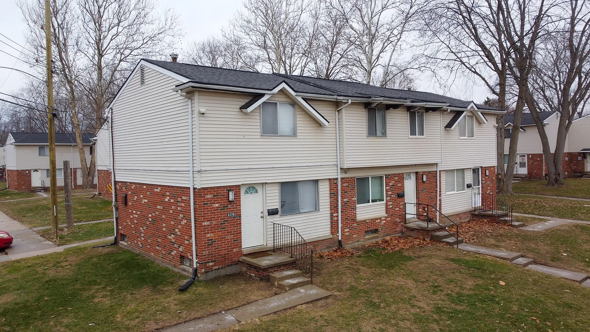 Charming two-story townhouse with brick facade, surrounded by lush green lawns and mature trees, offering a cozy residential ambiance.