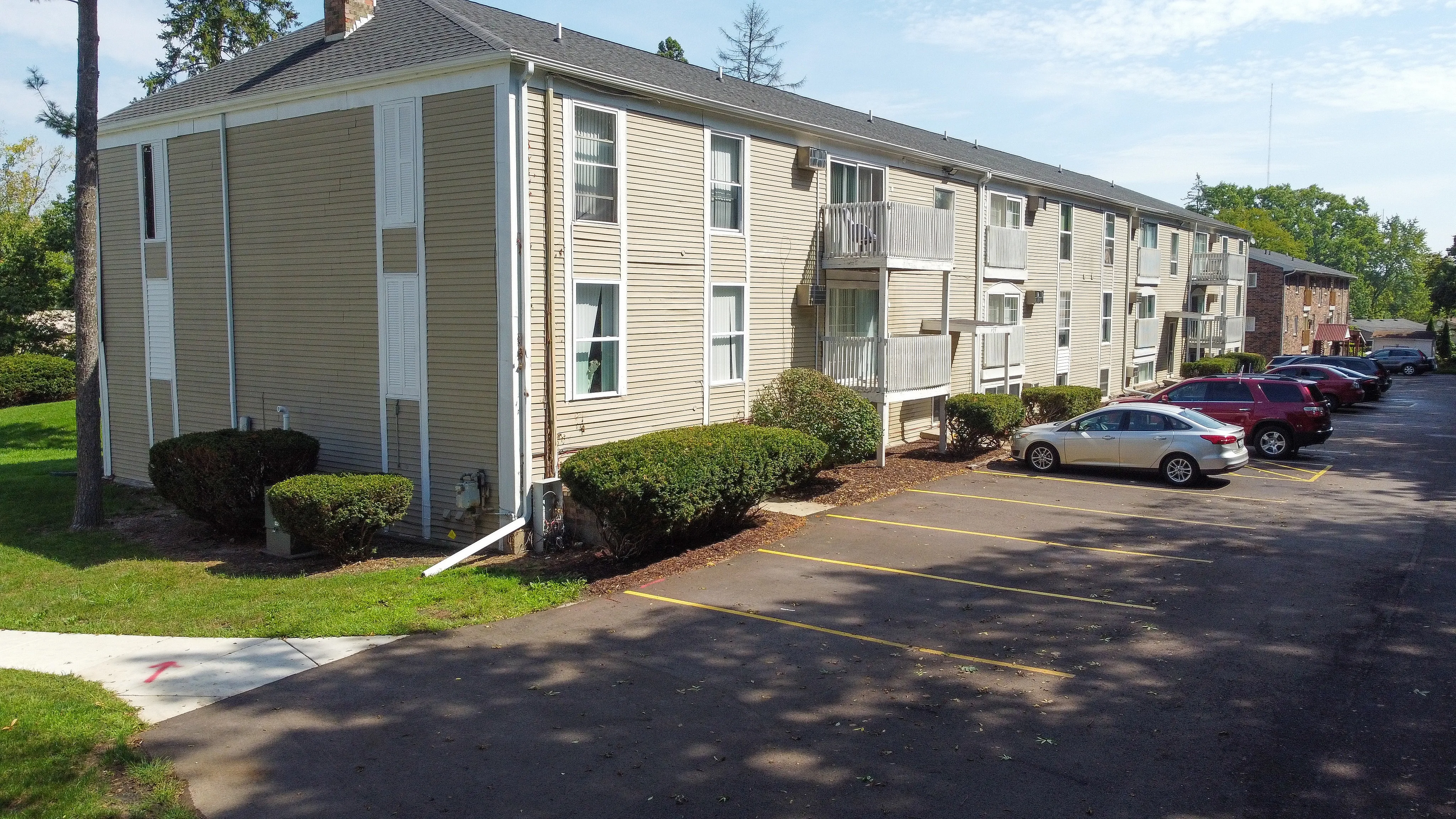 Charming apartment complex with spacious balconies, surrounded by lush greenery and ample parking space.
