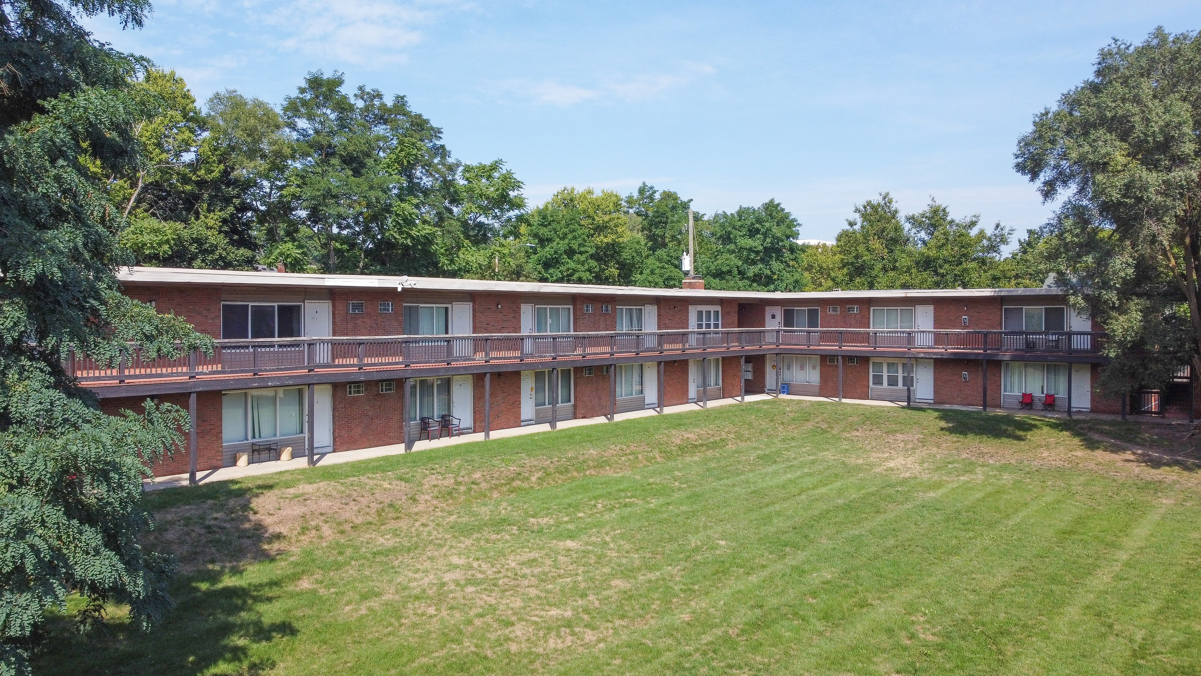 Charming brick apartment complex with lush green surroundings and expansive lawn, featuring spacious balconies perfect for enjoying a tranquil setting.