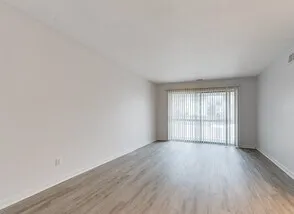 Spacious, sunlit living area with sleek hardwood floors and large window, offering a welcoming ambiance.