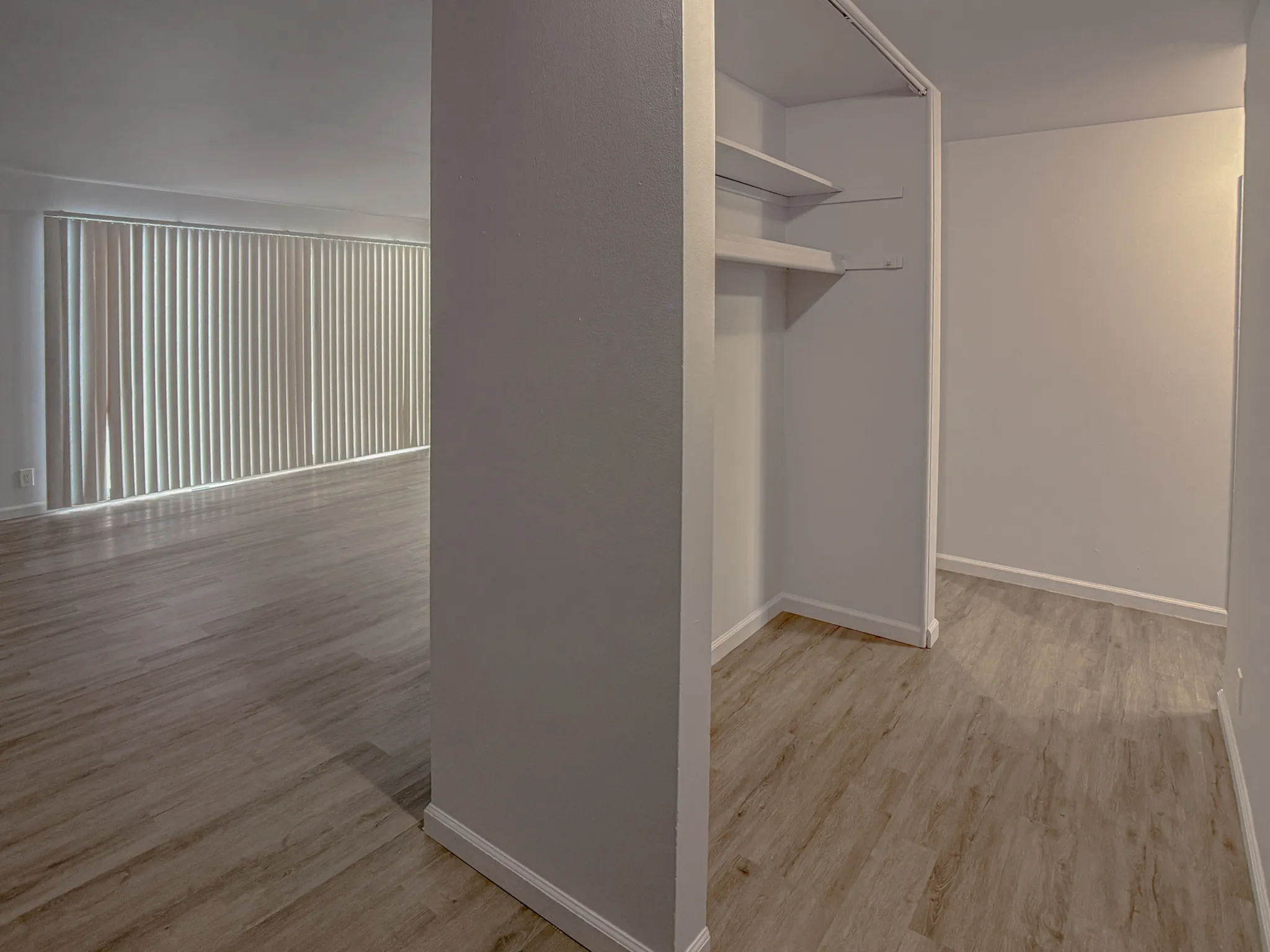 Spacious apartment interior featuring a large empty room with natural light, sleek flooring, and vertical blinds.