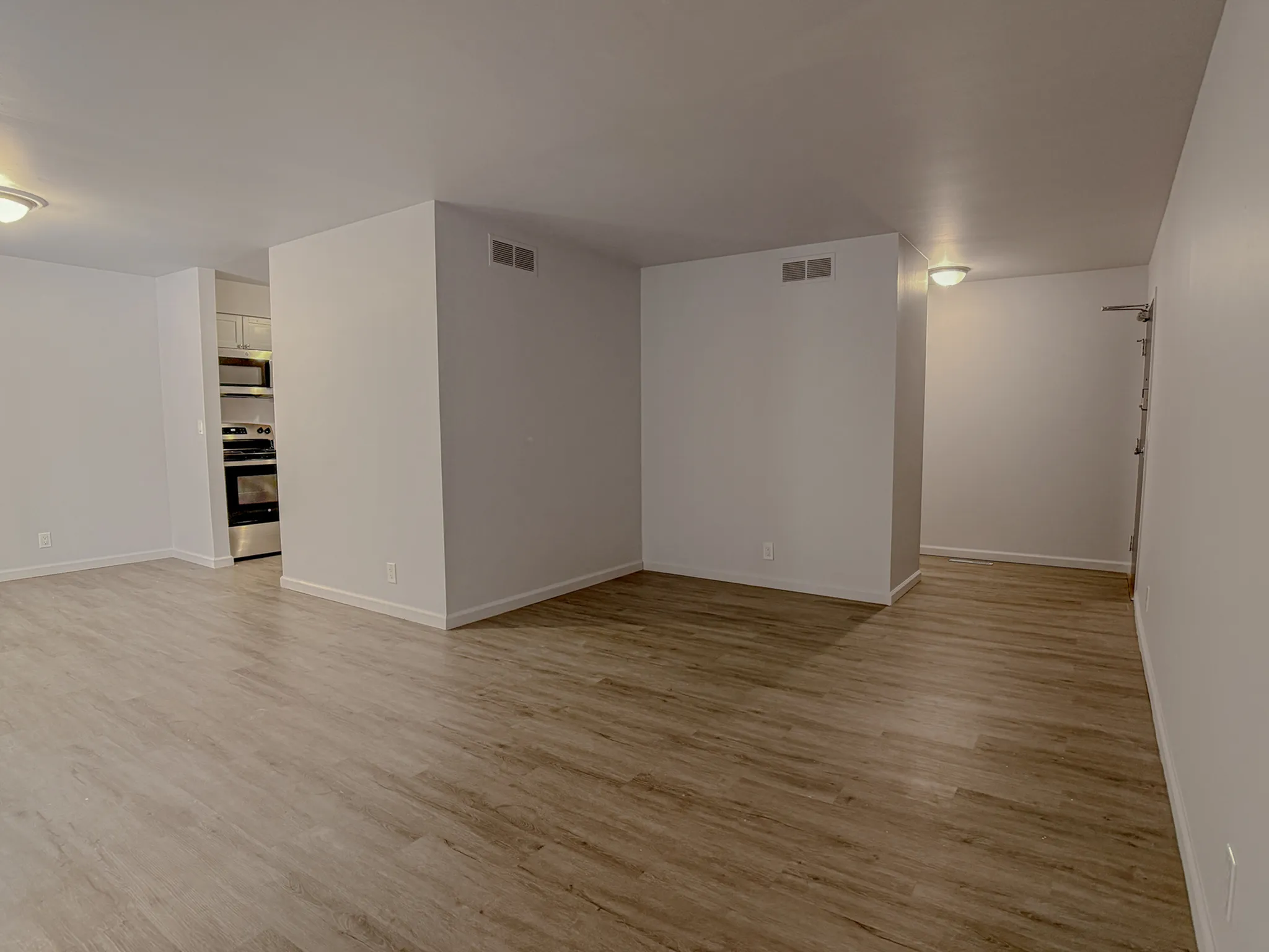 Modern open-concept living space with sleek hardwood floors and contemporary finishes leading to a bright kitchen area.