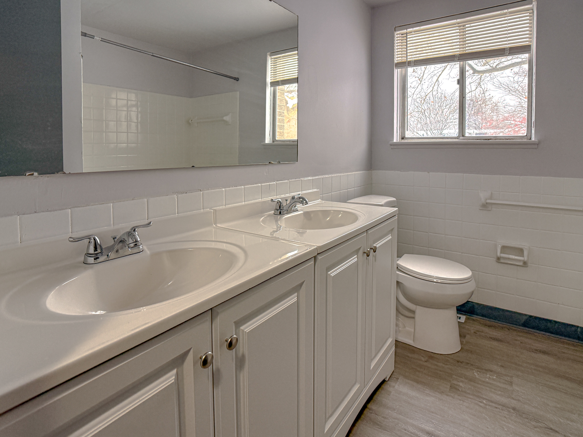 Bright and spacious bathroom featuring dual sinks and a large mirror, enhanced by ample natural light from the window.