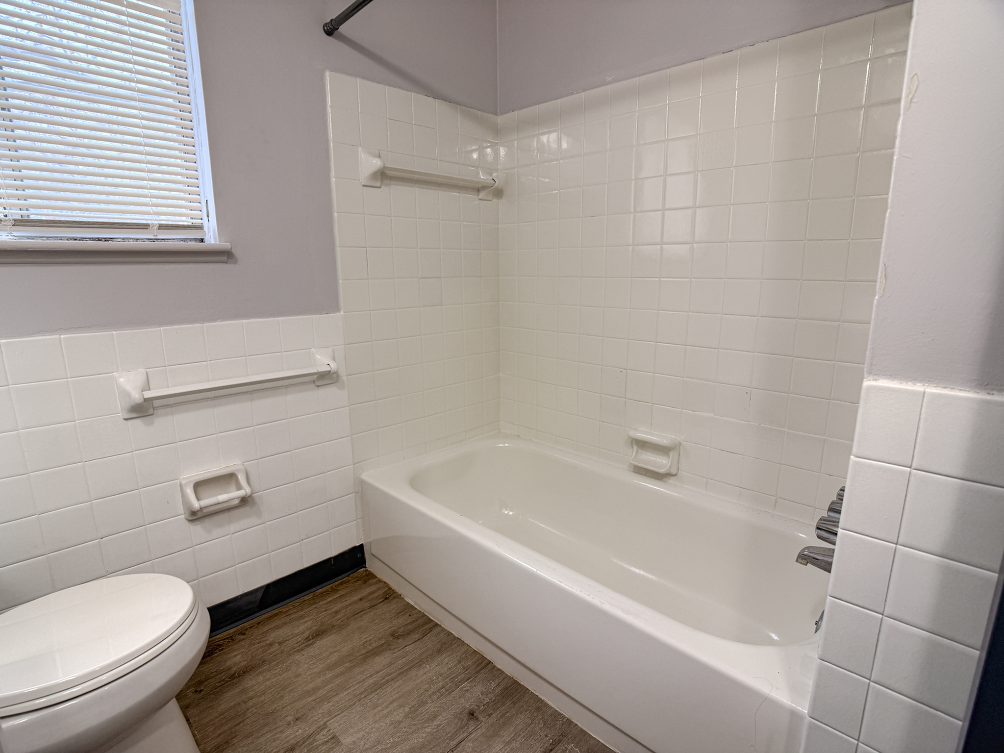 Modern bathroom with sleek white tiles, inviting bathtub, and natural light from a nearby window.