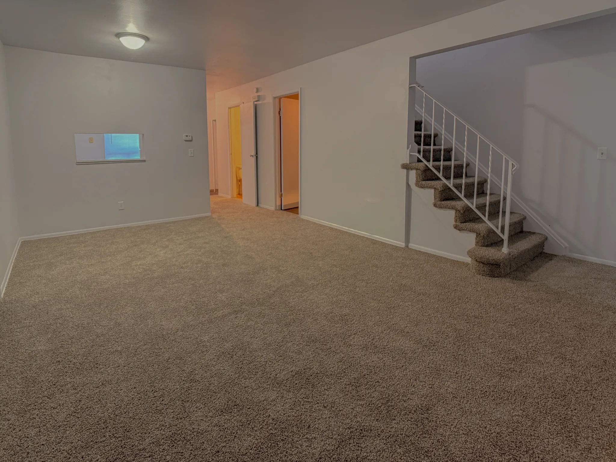 Spacious living area with plush carpeting and elegant staircase, perfect for modern comfort and style.