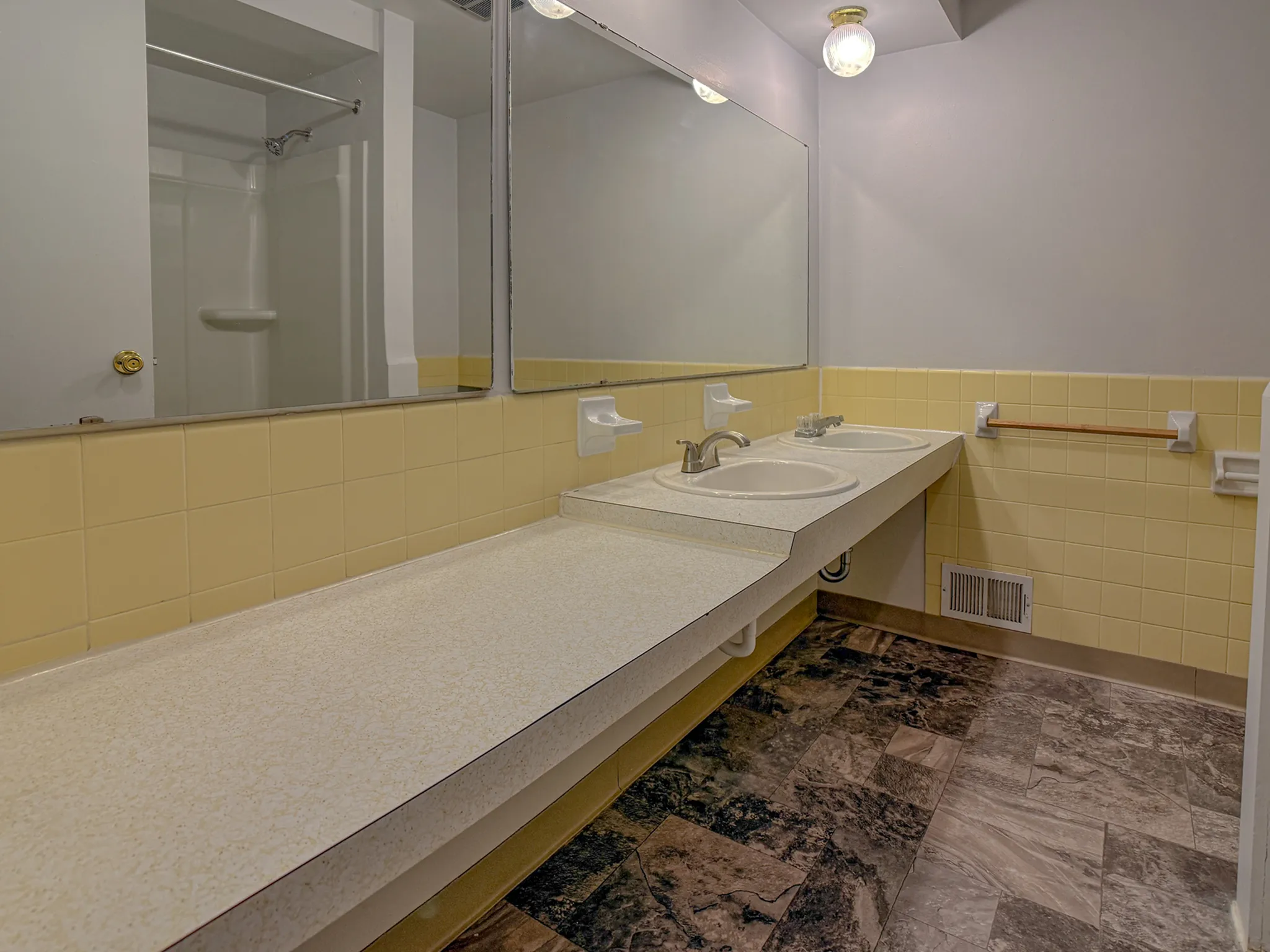 Spacious bathroom with dual sinks and elegant marble-style flooring, complemented by soft yellow tiles and ample countertop space.