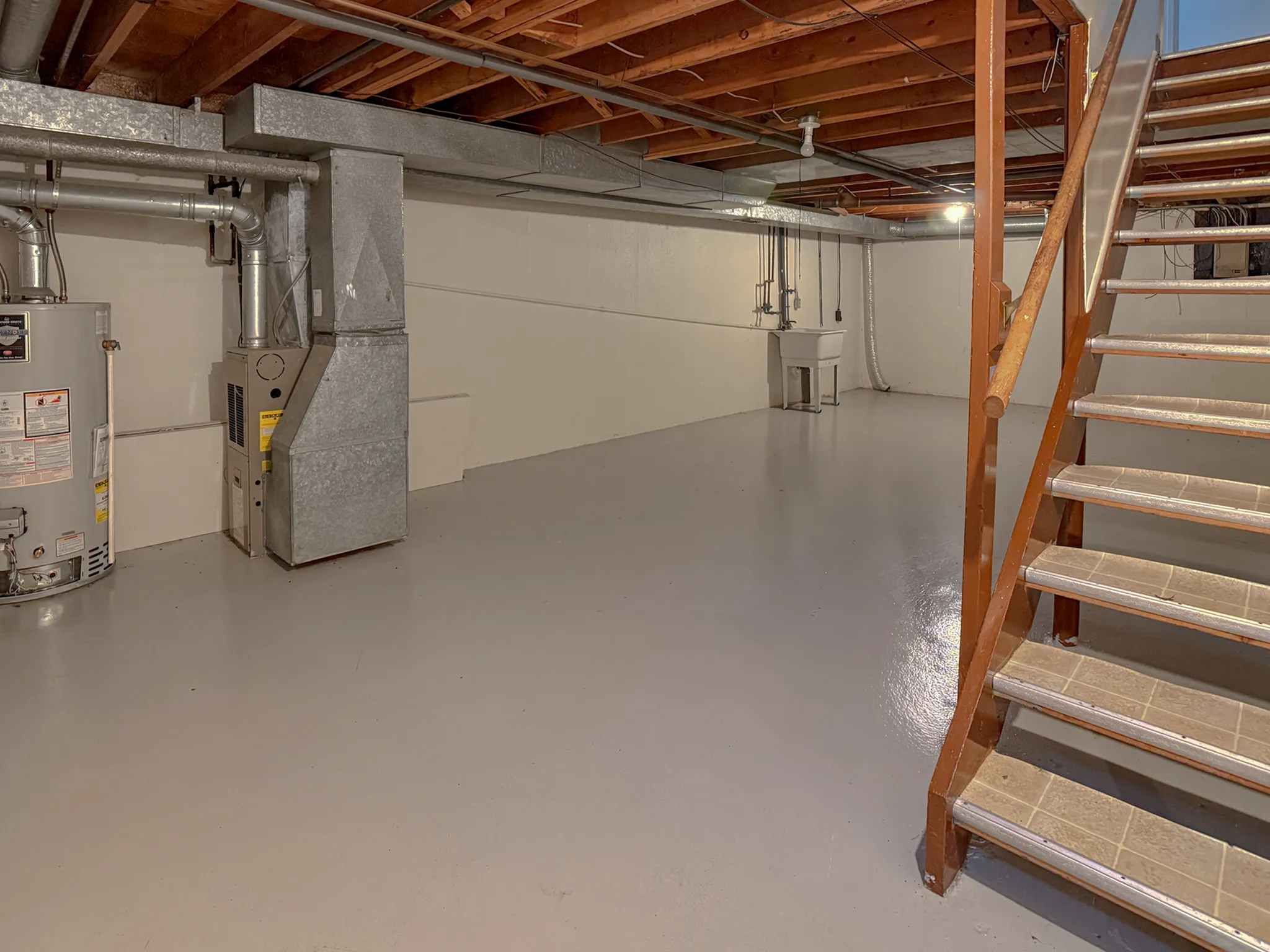 Spacious unfinished basement with potential for customization, featuring sturdy open stairs, a utility area, and bright lighting.