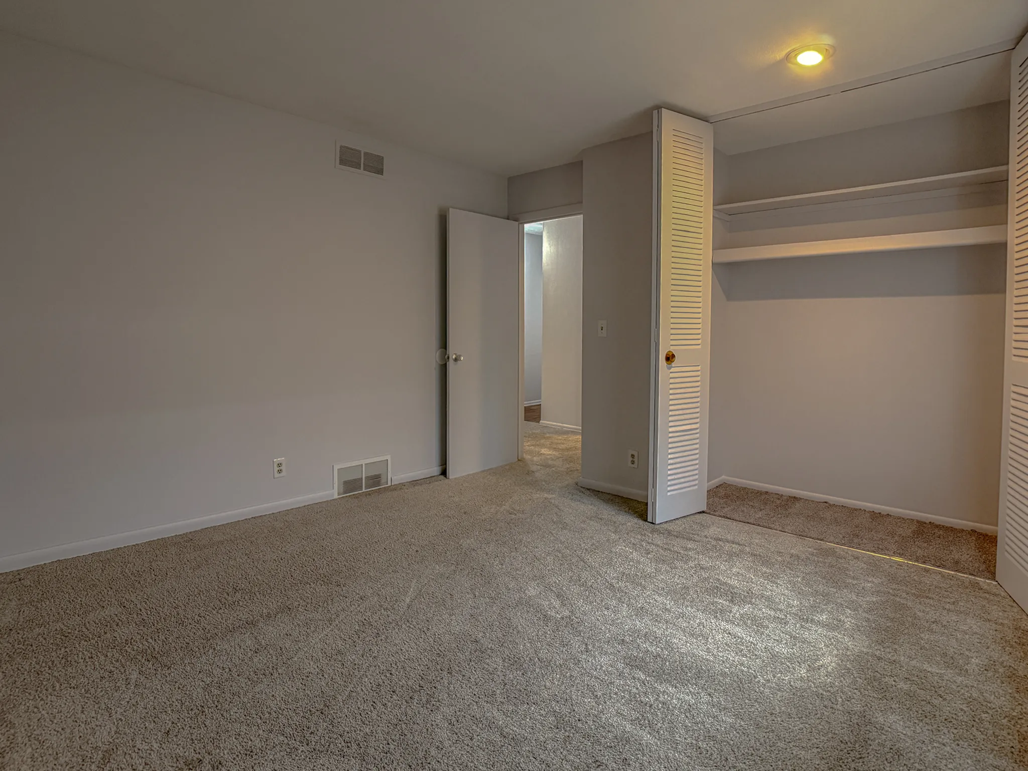 Spacious carpeted room with built-in closet, soft lighting, and neutral walls, perfect for a cozy retreat.
