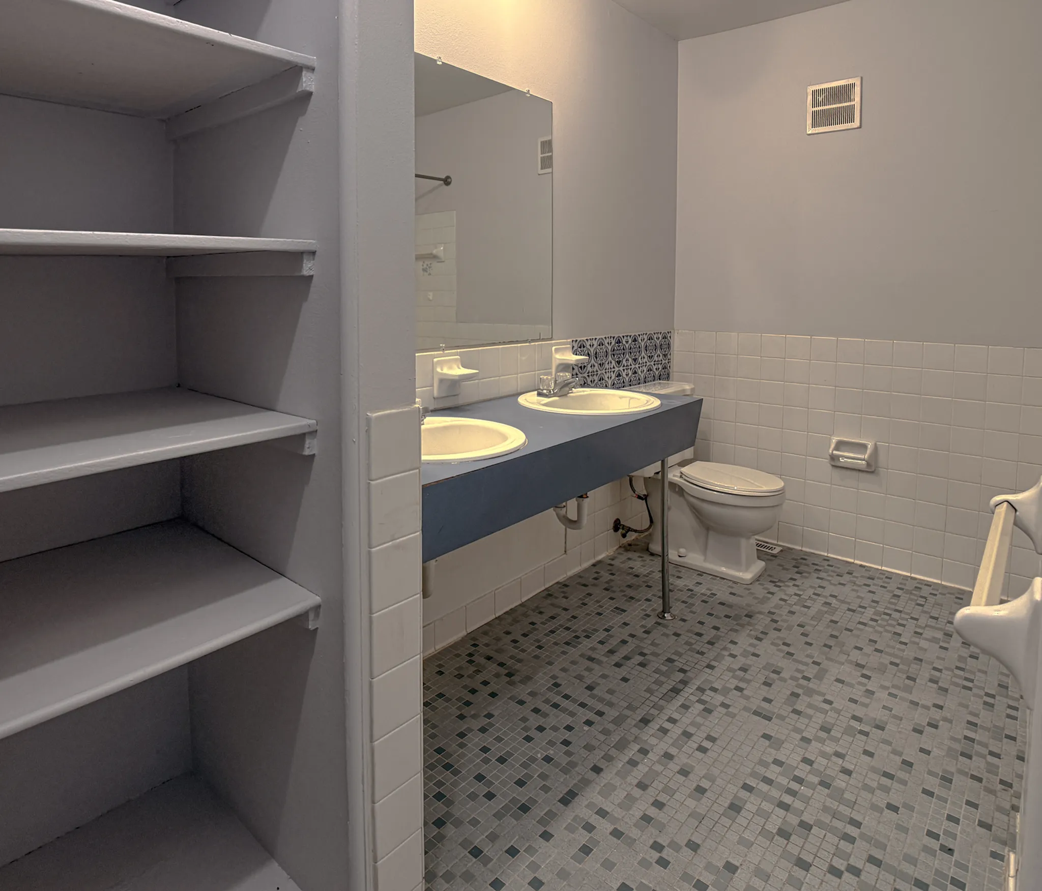 Spacious bathroom with dual sinks, elegant blue counter, and modern tile flooring, complemented by built-in shelving.