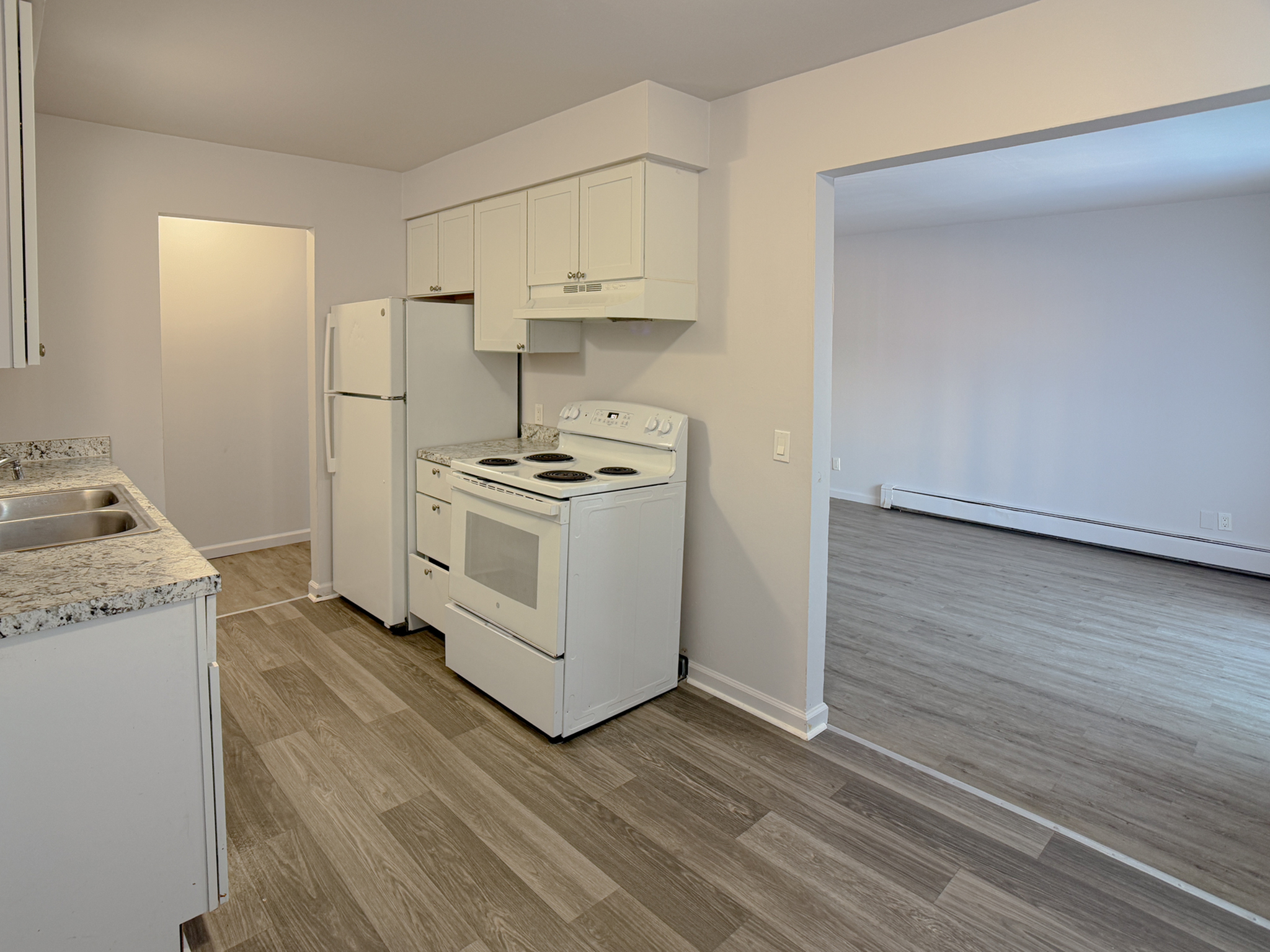 Modern open kitchen with white cabinetry leading to bright living area, featuring sleek flooring and contemporary appliances.