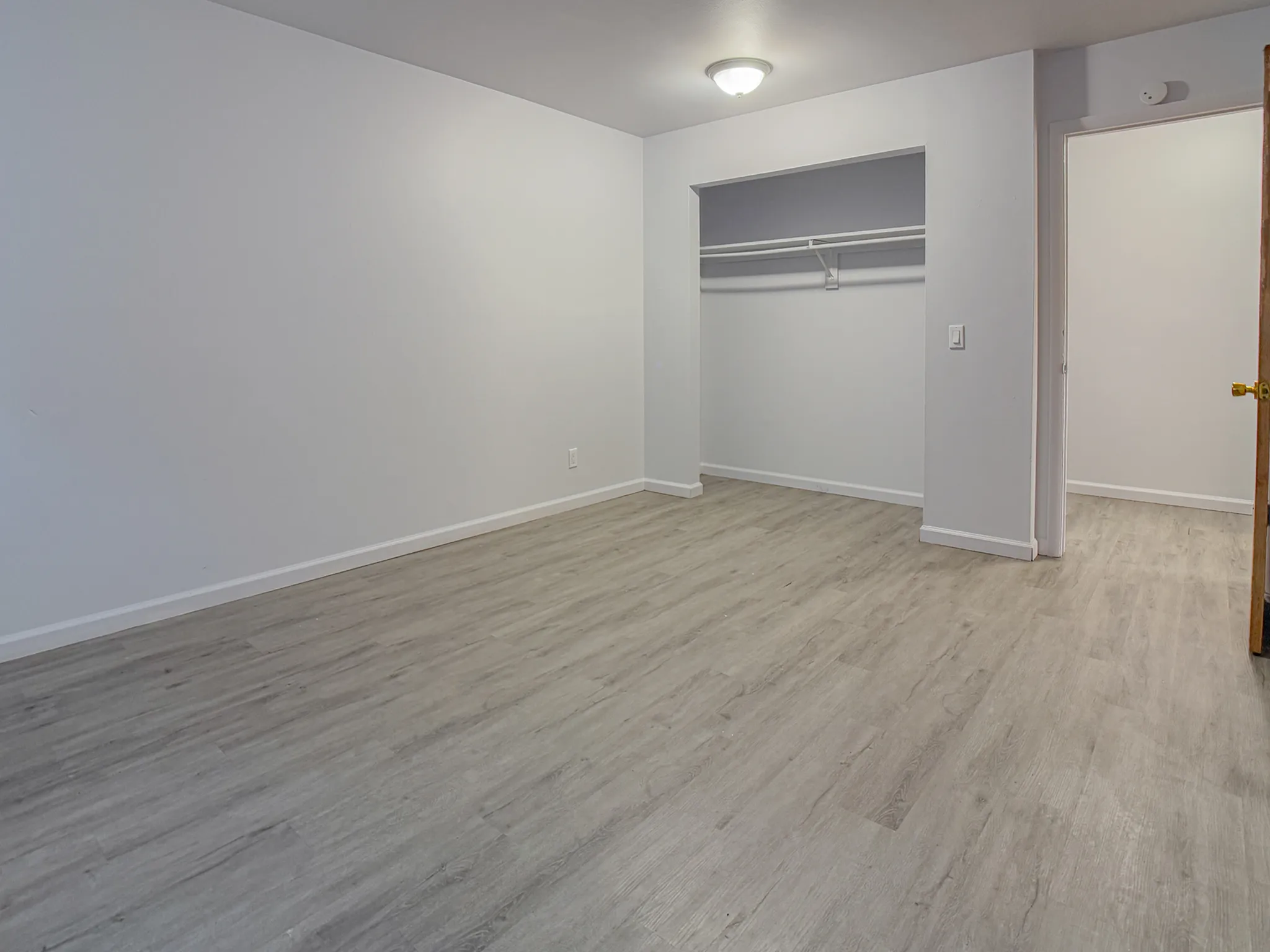Sleek, modern bedroom with spacious closet and fresh, bright paint accentuating wood-style flooring.