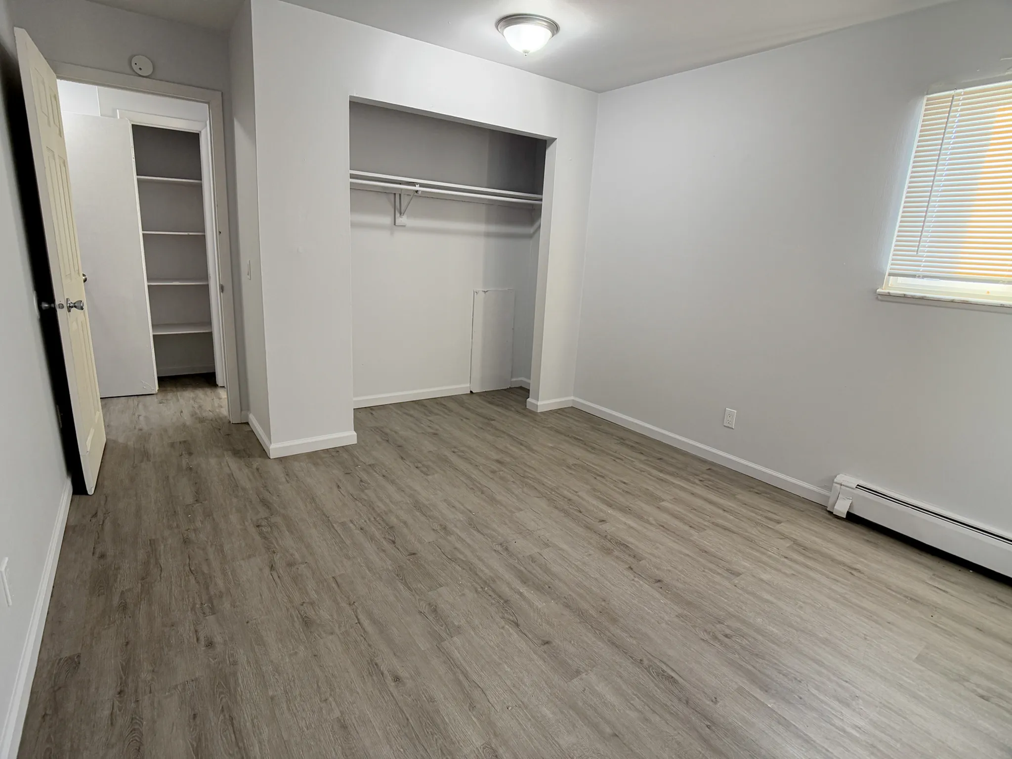 Inviting bedroom with spacious walk-in closet and large window, featuring elegant wood flooring and neutral walls.