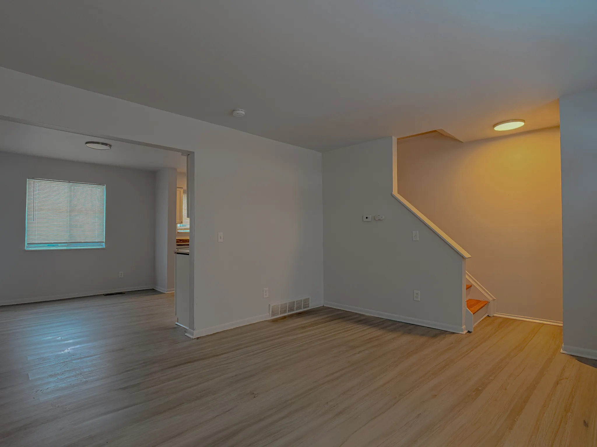 Inviting open-plan living space with modern laminate flooring, ample natural light, and a cozy stairway leading to the upper floor.