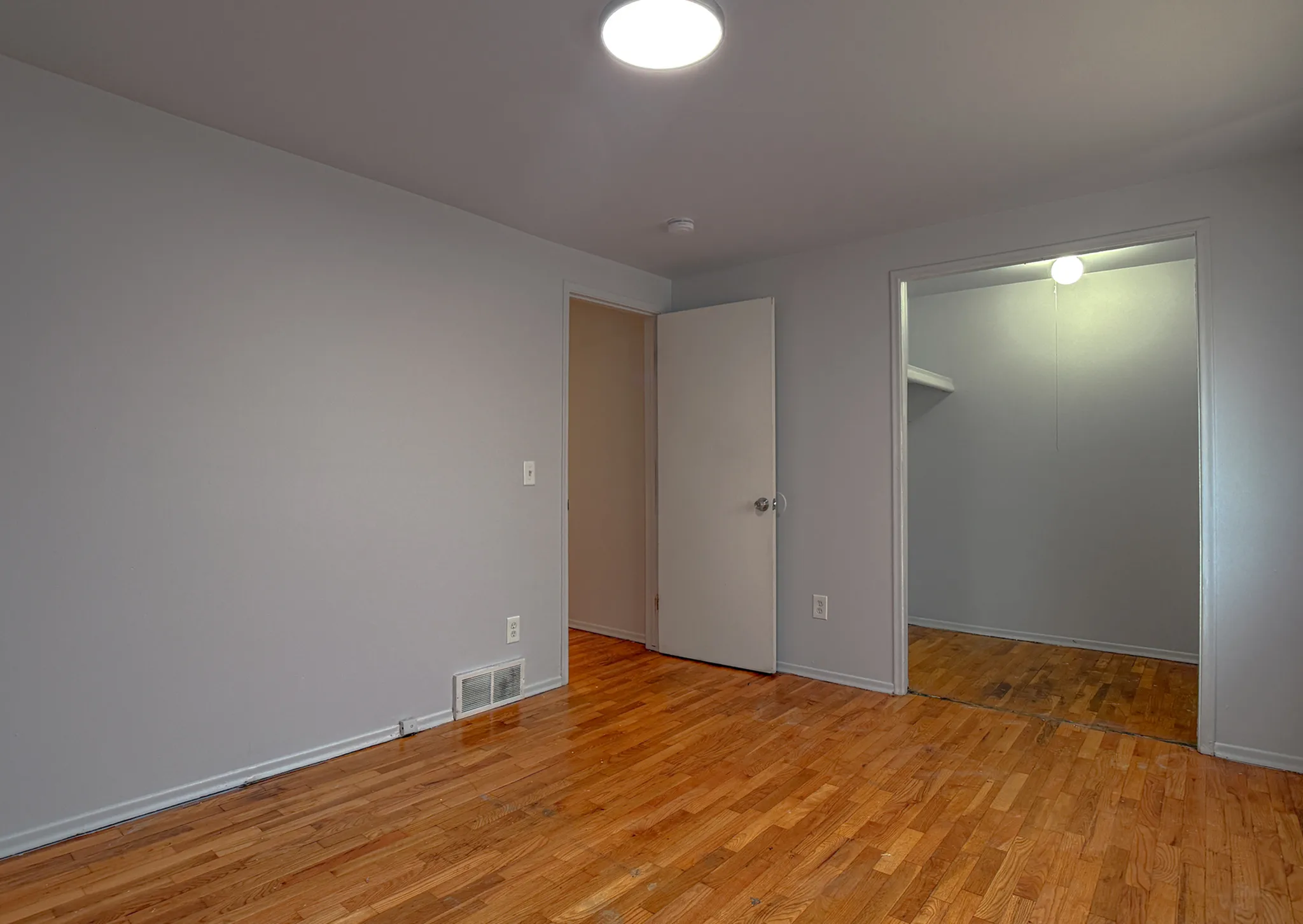 Inviting empty room featuring polished hardwood floors and a spacious walk-in closet ready for customization.