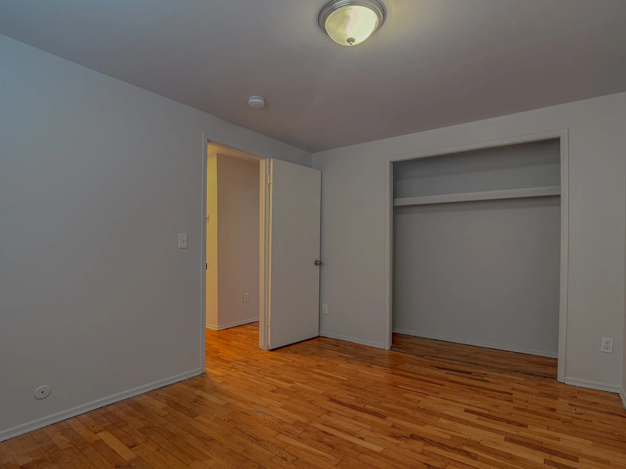 Charming bedroom with hardwood floors and a spacious open closet, featuring a bright overhead light and neutral walls.