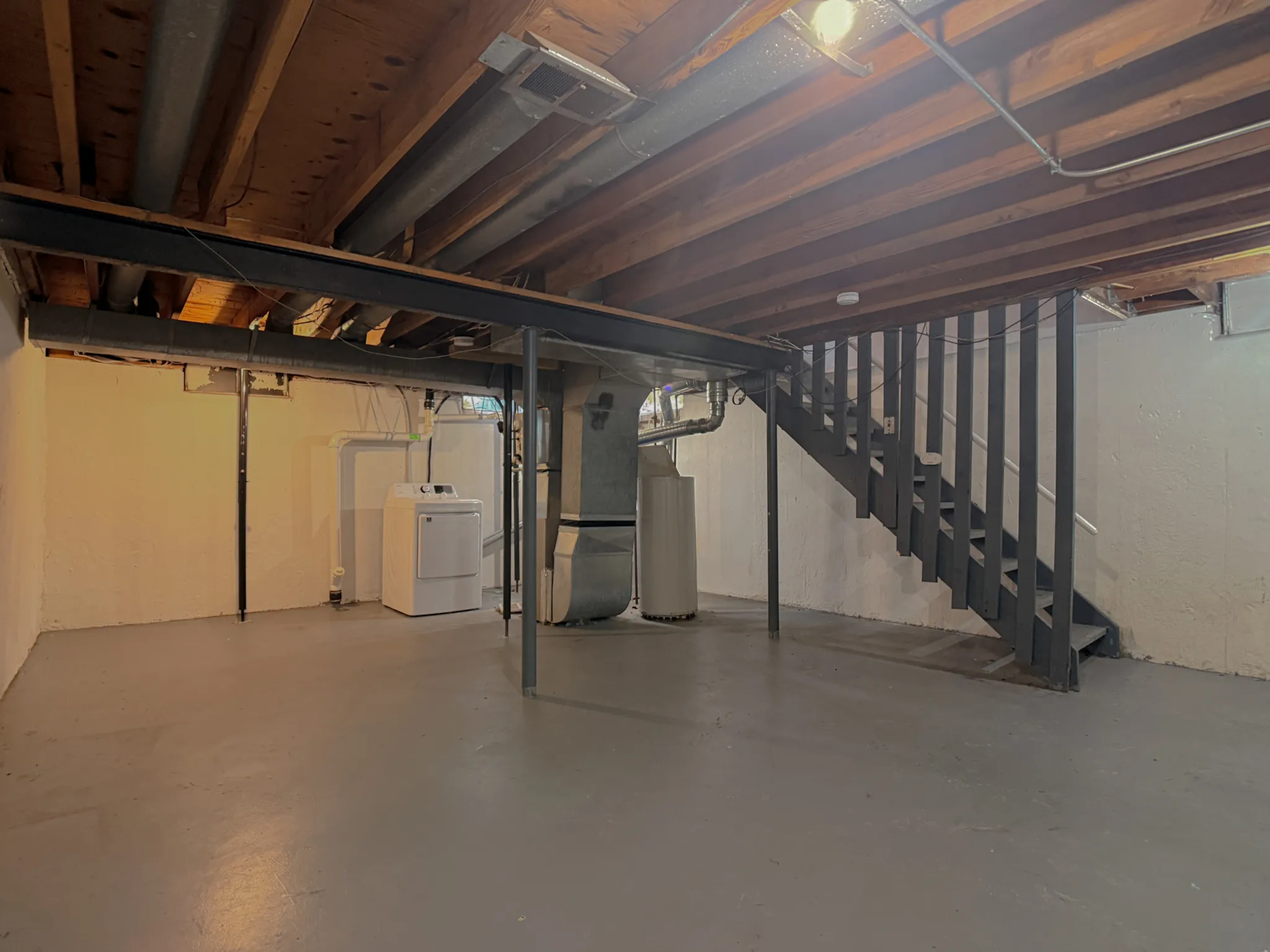 Spacious unfinished basement with modern utility setup, featuring a washer and dryer, exposed beams, and ample storage space.