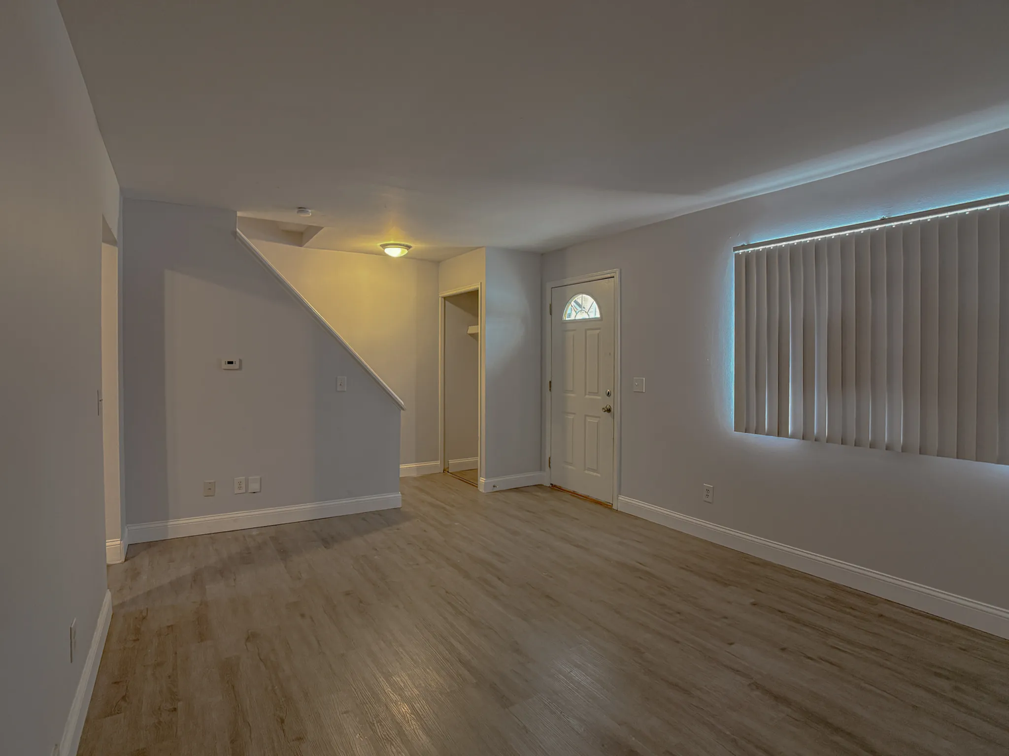 Modern living space featuring elegant wood flooring, ambient lighting, and a charming door entrance with vertical blinds for a cozy atmosphere.