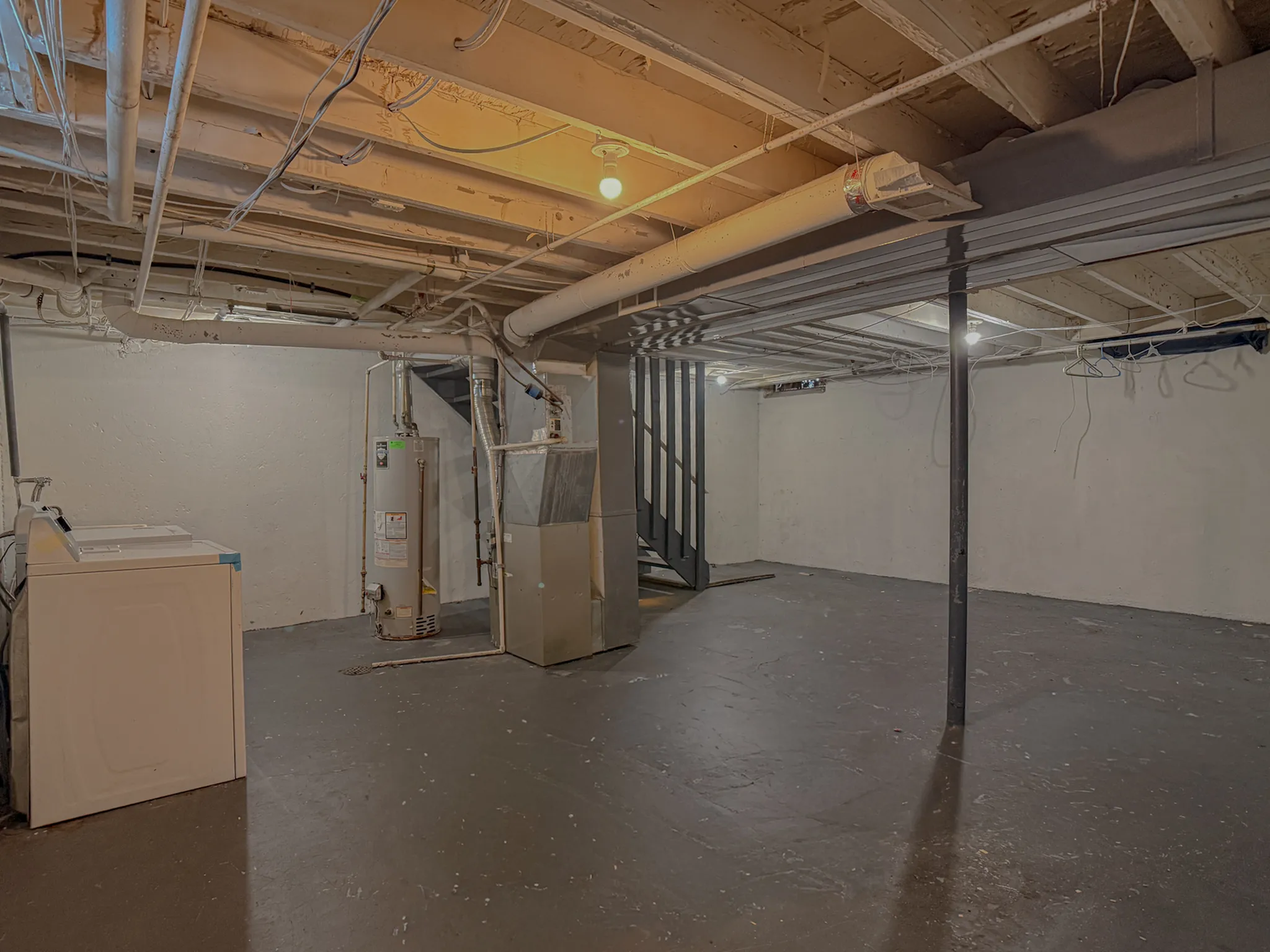 Spacious unfinished basement featuring exposed beams, a water heater, and laundry area with washer.