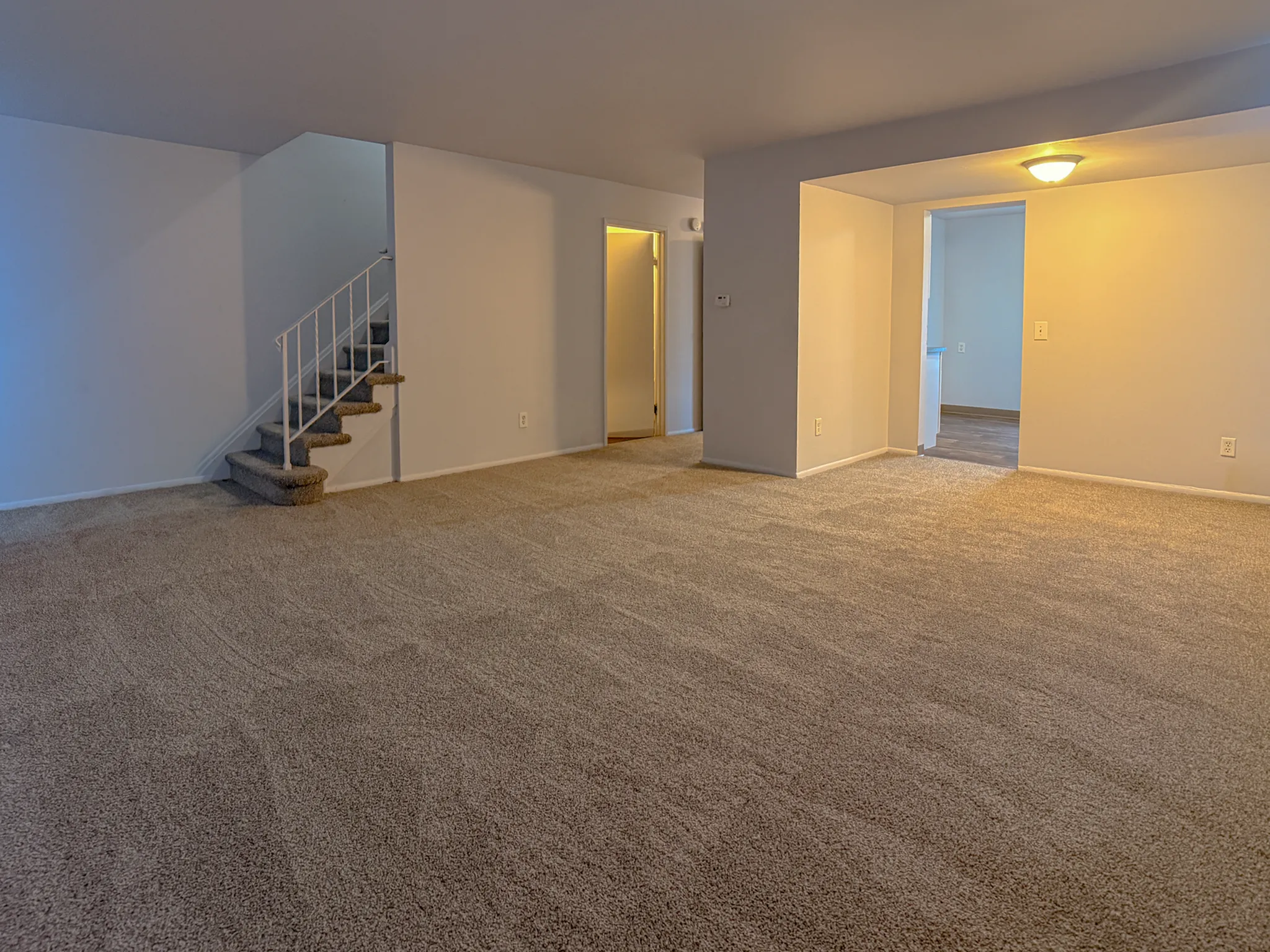 Inviting open living space with plush carpeting and cozy staircase leading to upper floor.