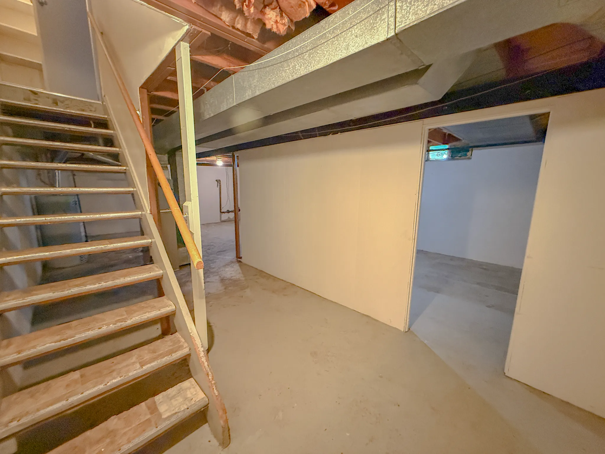 Spacious basement with unfinished potential, featuring wooden stairs and partially completed walls, ideal for customization.