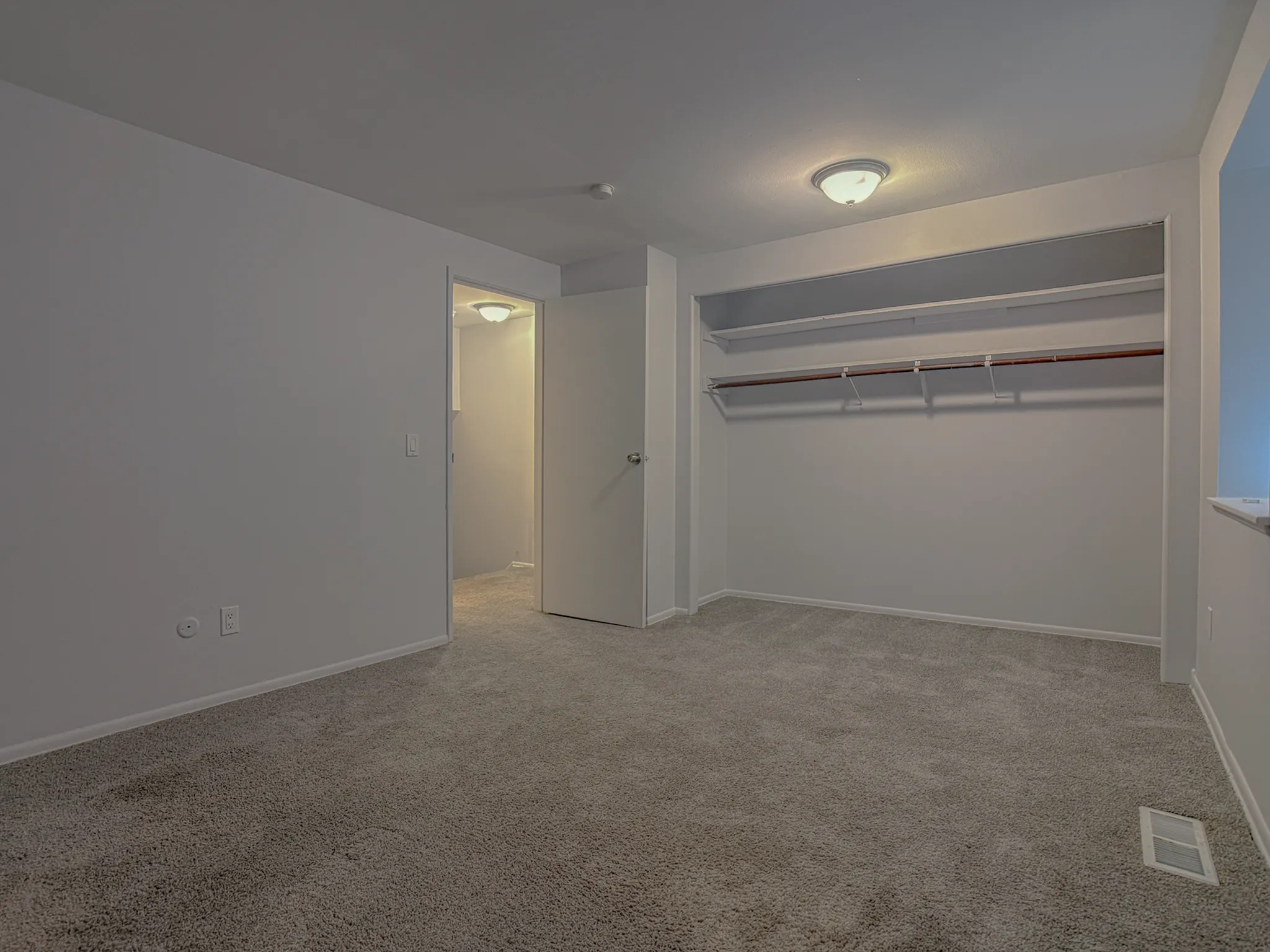 Inviting bedroom with plush carpet, open closet space, and soft overhead lighting in a modern apartment.