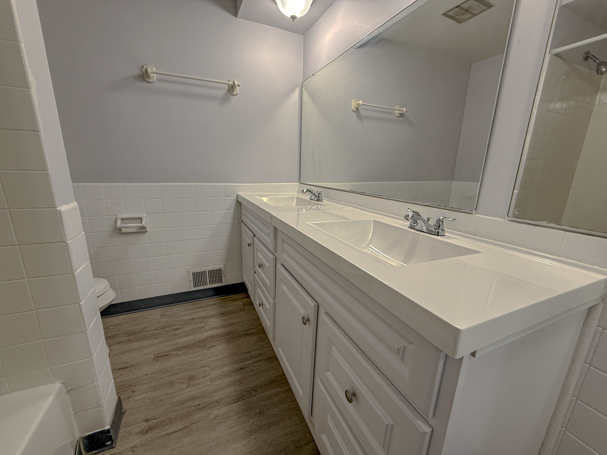 Modern bathroom featuring dual sinks, large mirror, and elegant cabinetry with sleek flooring.