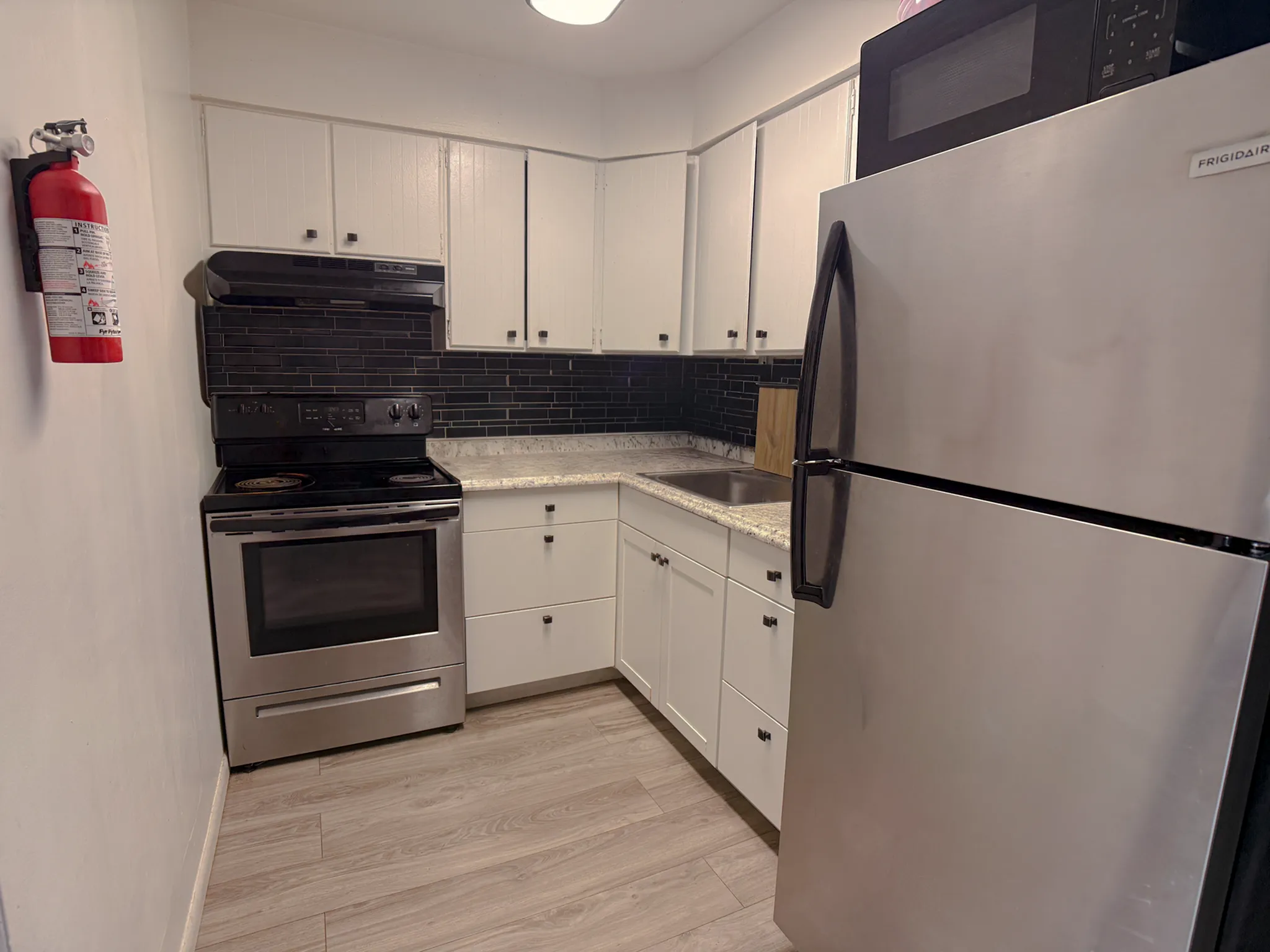 Modern kitchen featuring sleek stainless steel appliances, elegant black backsplash, and wood flooring.
