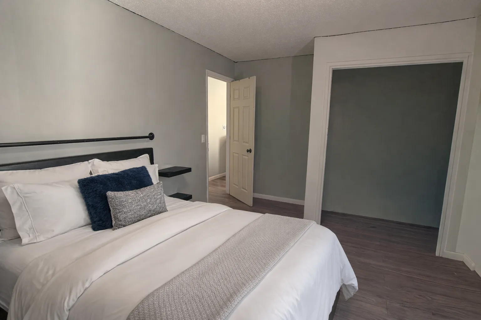 Inviting bedroom with a cozy bed, sleek shelves, and rich wooden flooring, emanating warmth and comfort.