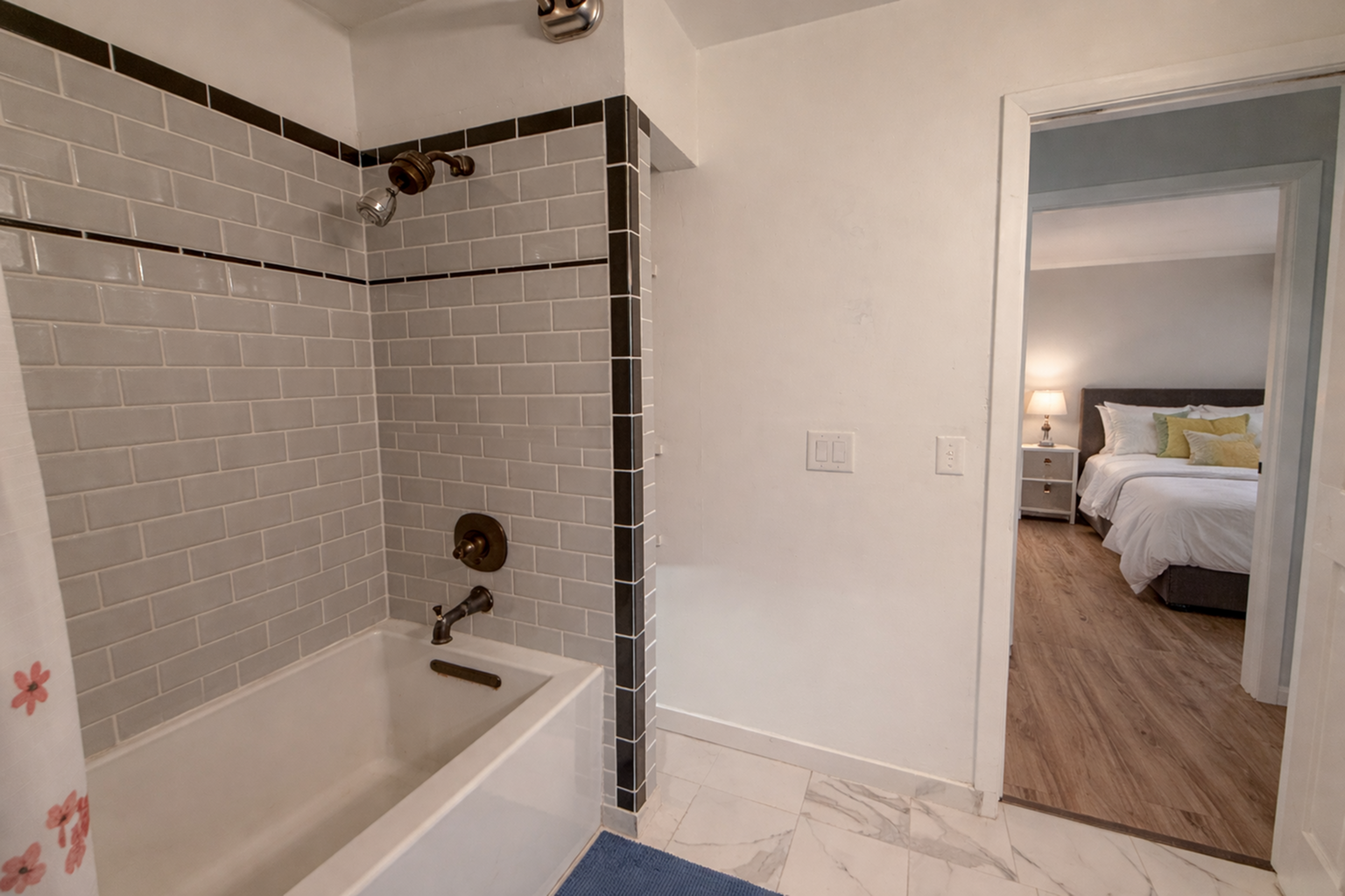 Modern bathroom with tiled shower and view into cozy bedroom with warm lighting.