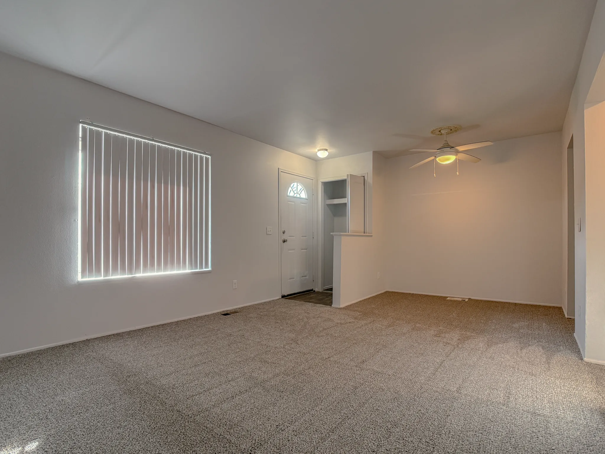 Inviting living room with plush carpet, ceiling fan, and natural light filtering through vertical blinds.