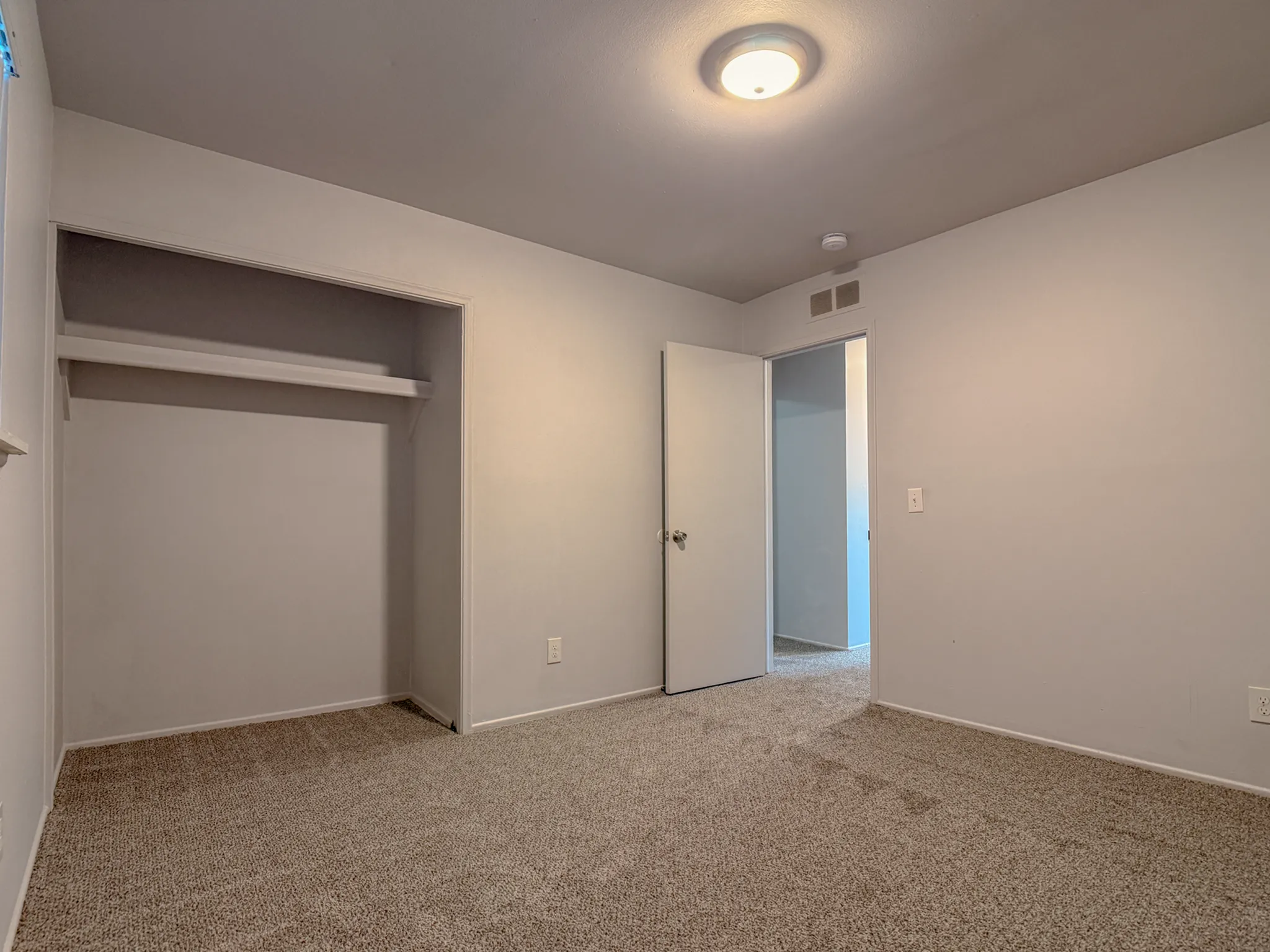 Spacious and inviting bedroom with a cozy carpet, built-in closet, and soft overhead lighting.
