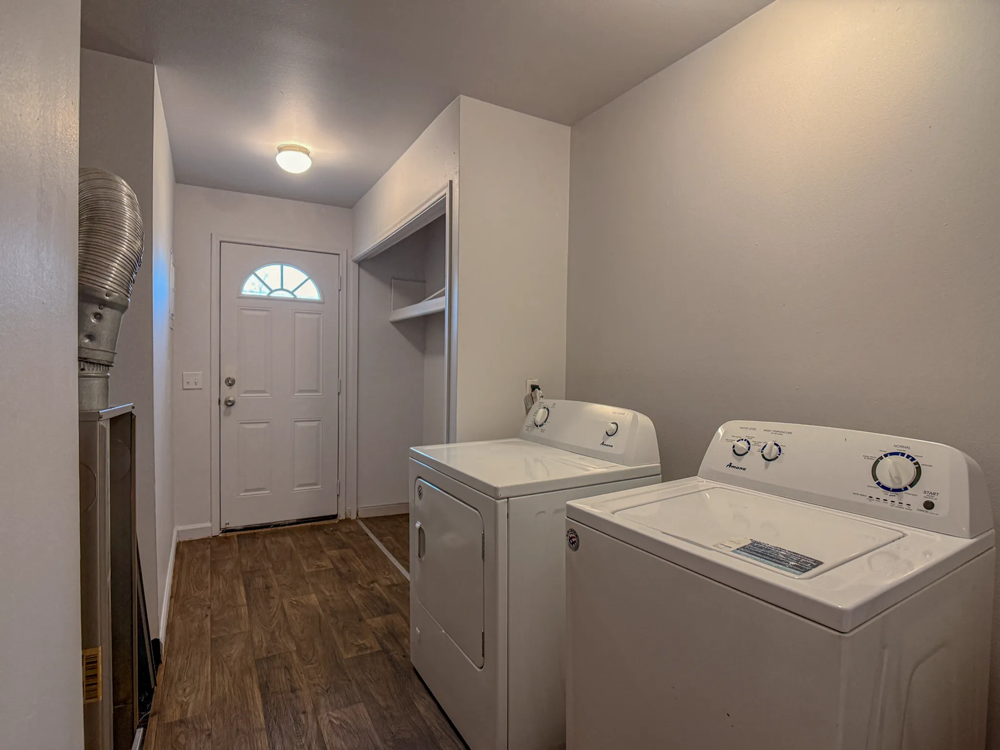 Charming laundry room with modern washer and dryer, featuring elegant wood flooring and ample shelving.
