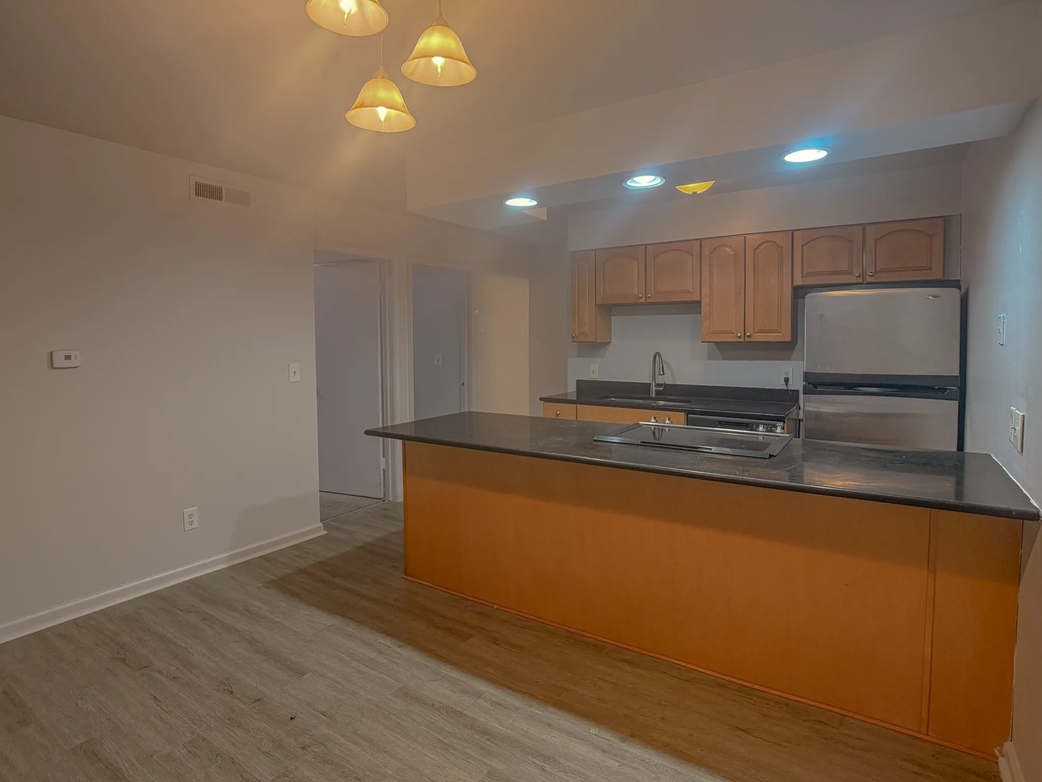 Contemporary kitchen with sleek black countertops, stainless steel appliances, and warm wooden cabinetry under ambient lighting.