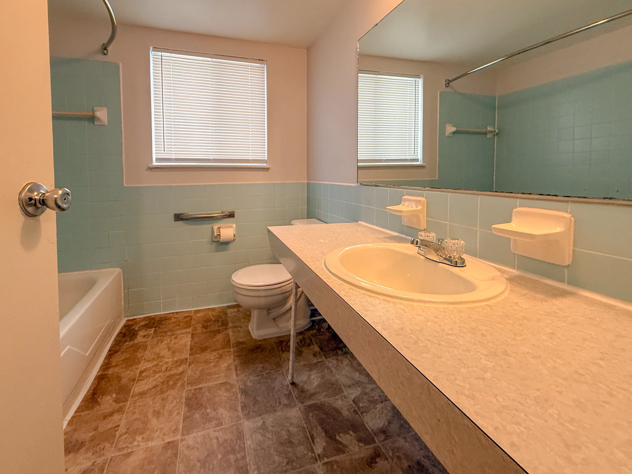 Bright and airy bathroom with vintage blue tiles, a large mirror, and natural light from the window.