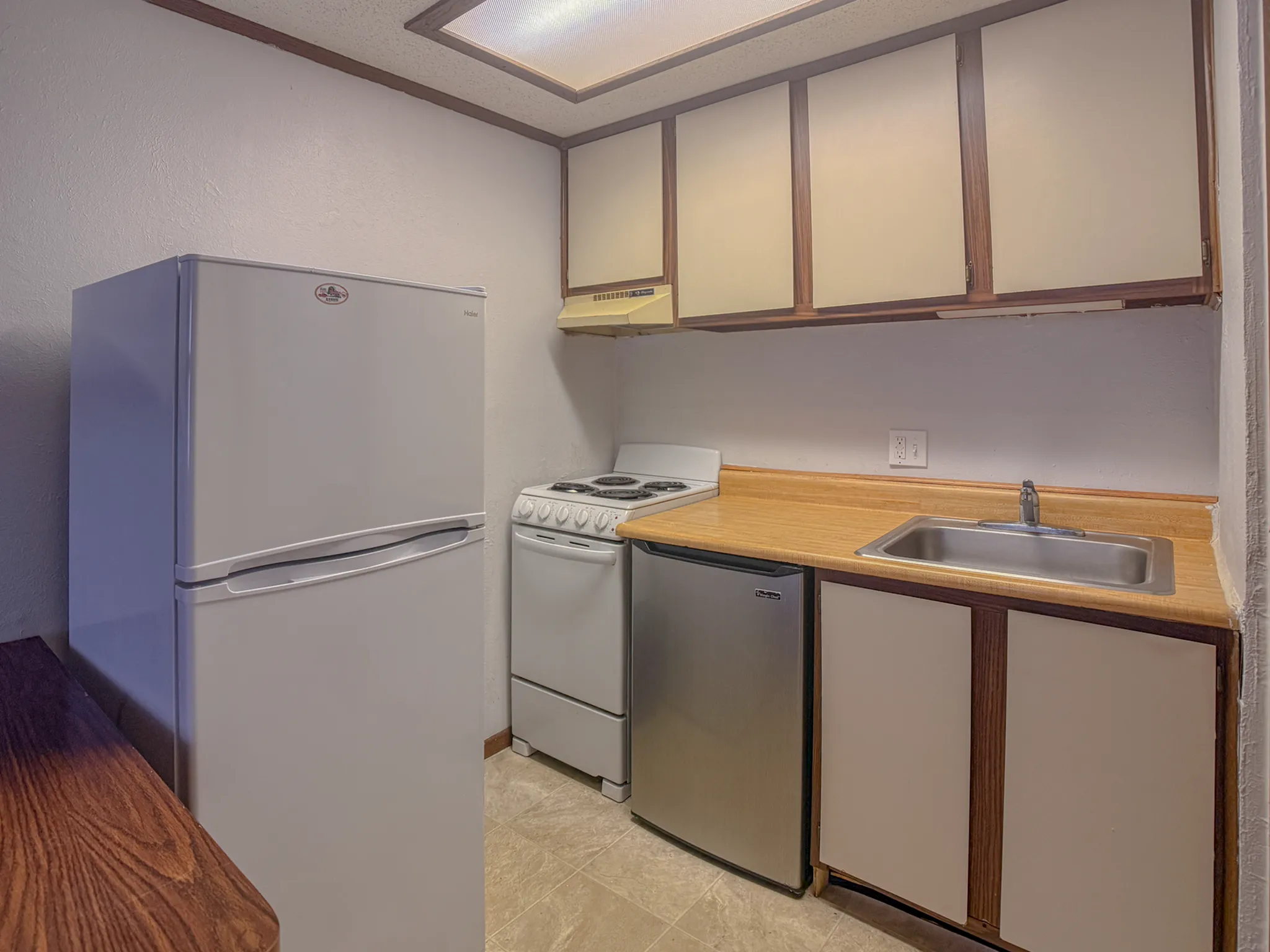 Cozy kitchen space featuring modern refrigerator, compact stove, and stylish wood cabinets.