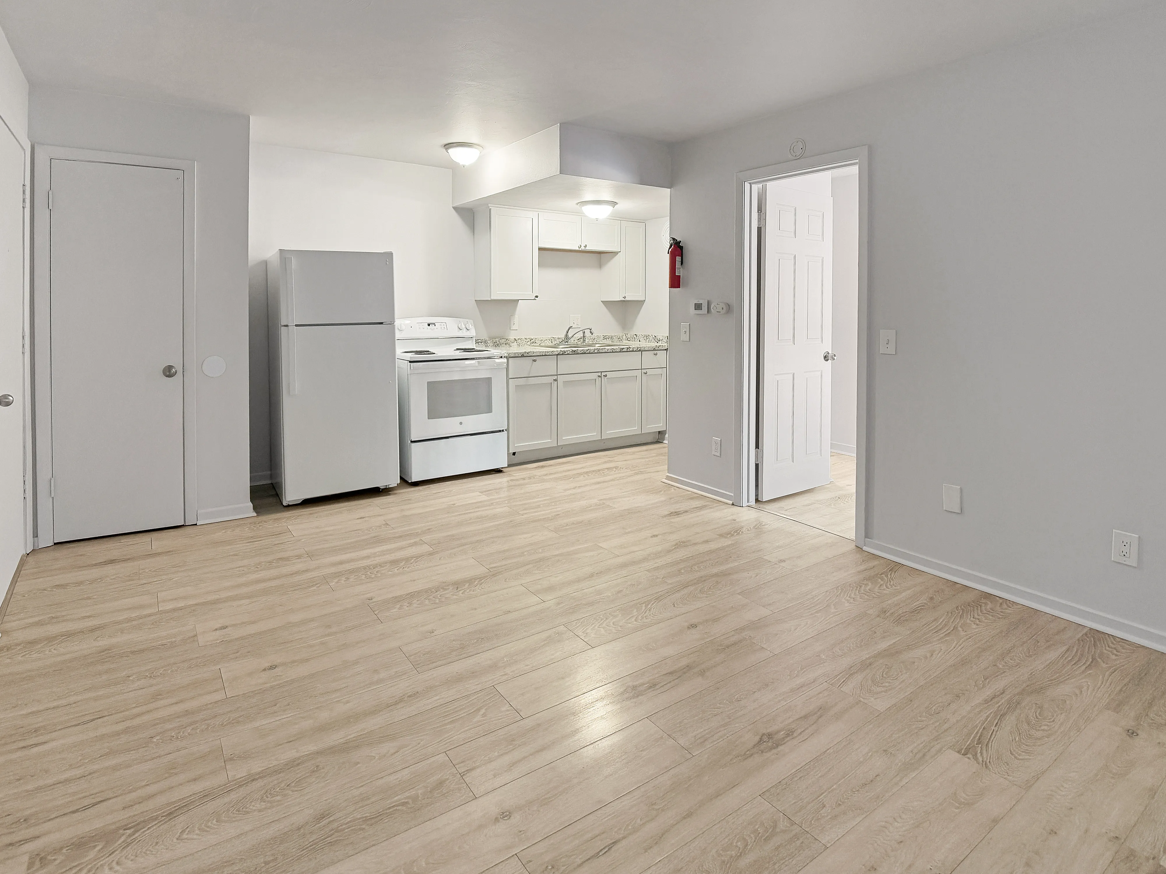 Modern apartment kitchen featuring sleek white cabinetry, contemporary appliances, and elegant wood flooring.