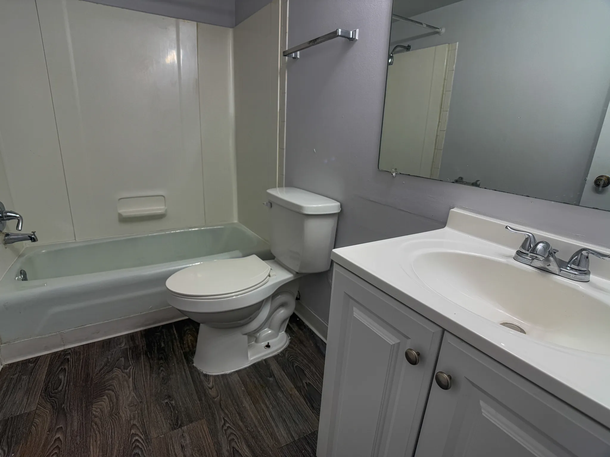 Modern bathroom featuring elegant wood-look flooring, a sleek white vanity with ample storage, large wall mirror, and a cozy bathtub.